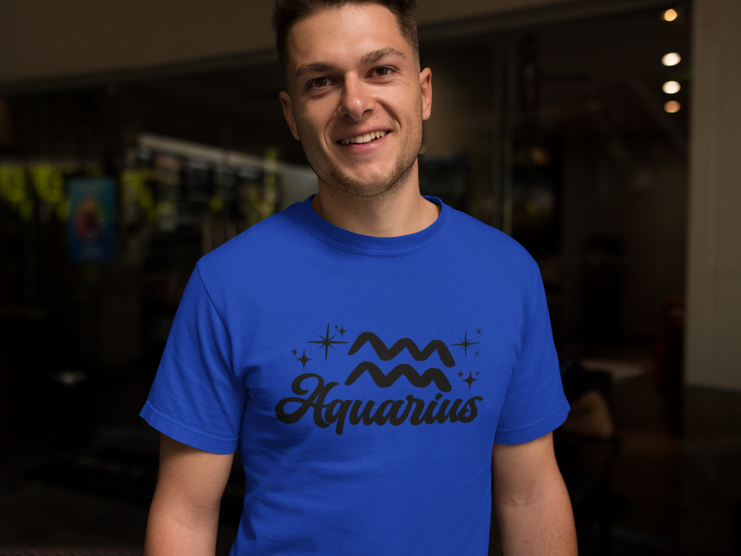Person wearing a blue t-shirt with 'Aquarius' black text design in a dark indoor setting