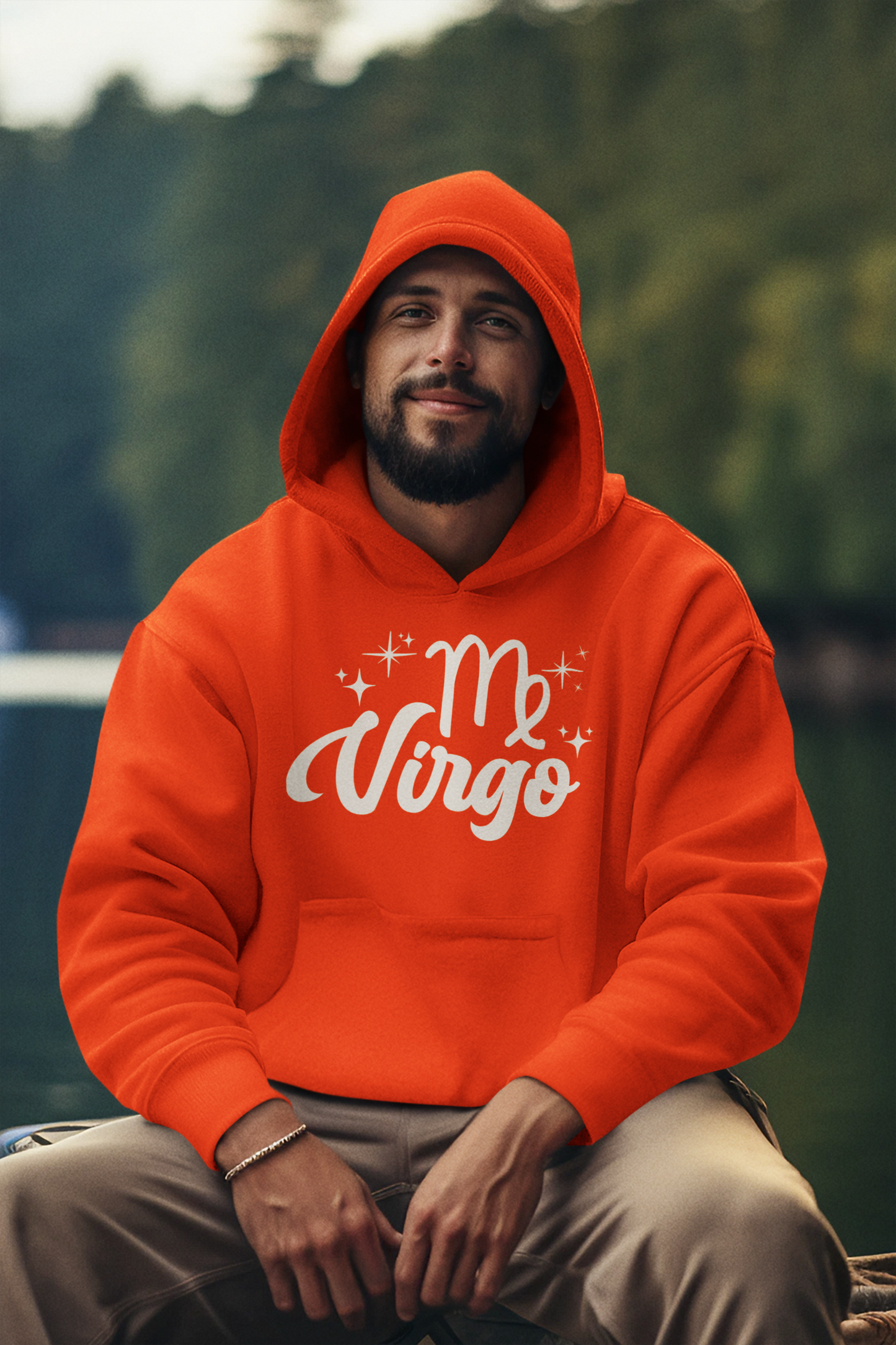 Man wearing a orange hoodie with 'Virgo' white text design, sitting outdoors with a blurred natural background