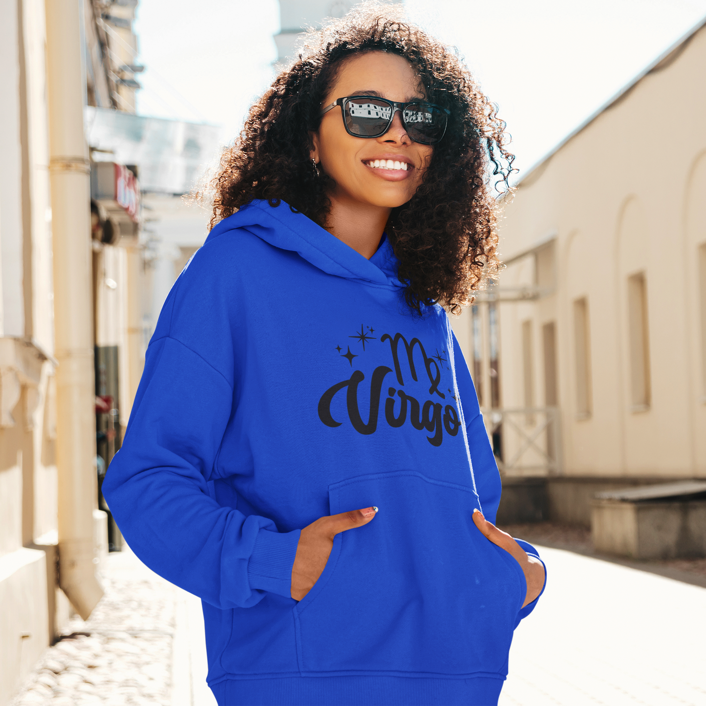 Woman with sunglasses, wearing a blue hoodie with "Virgo' black text design standing on the street.