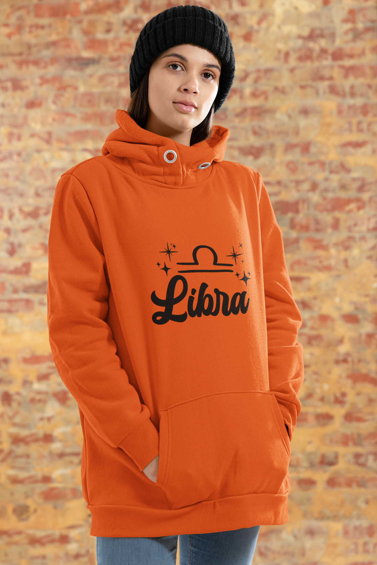 Person wearing a orange hoodie with 'Libra' black text design standing in front of a brick wall.