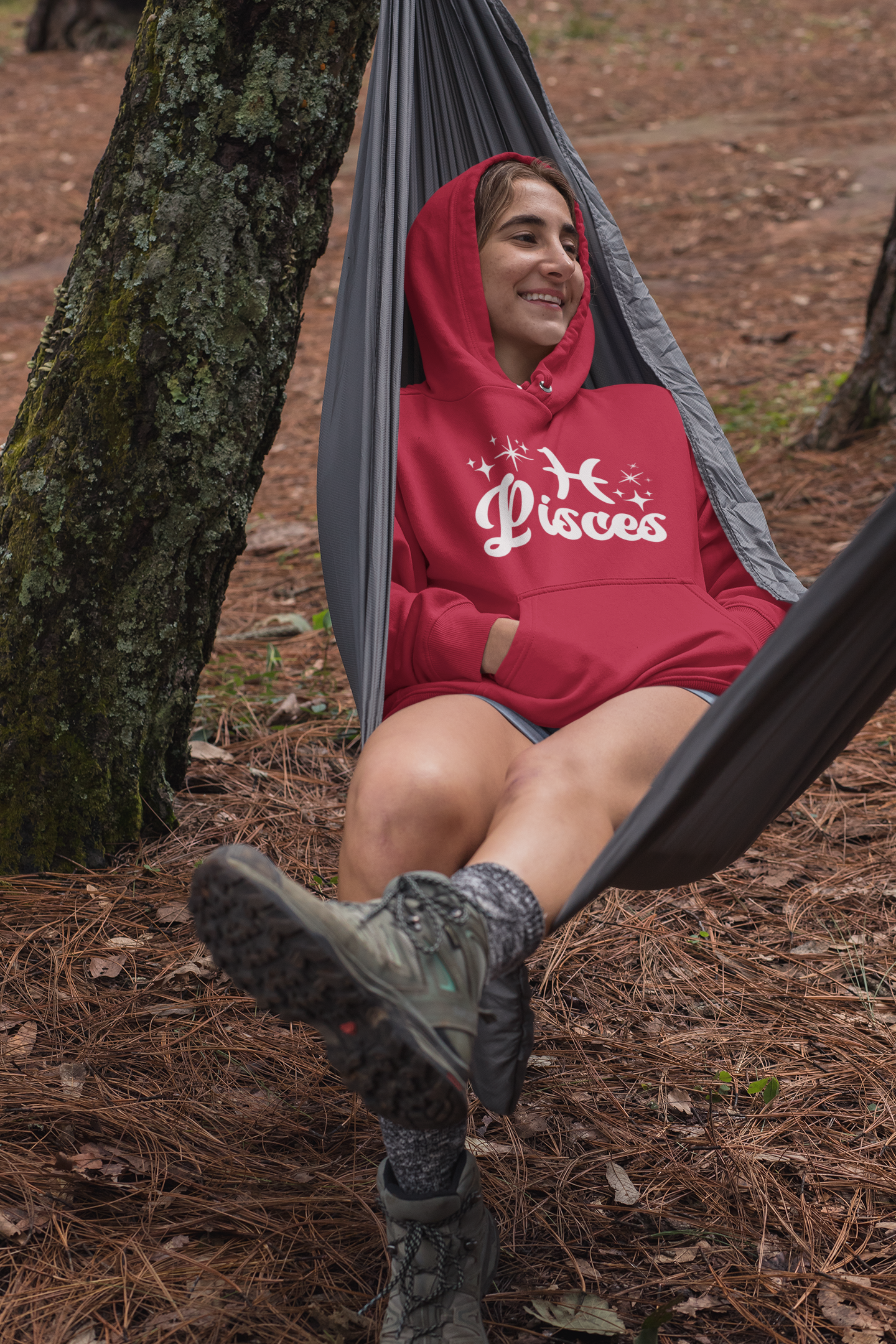 Person sitting in a hammock outdoors wearing a red hoodie with 'Pisces' white text with zodiac symbol.