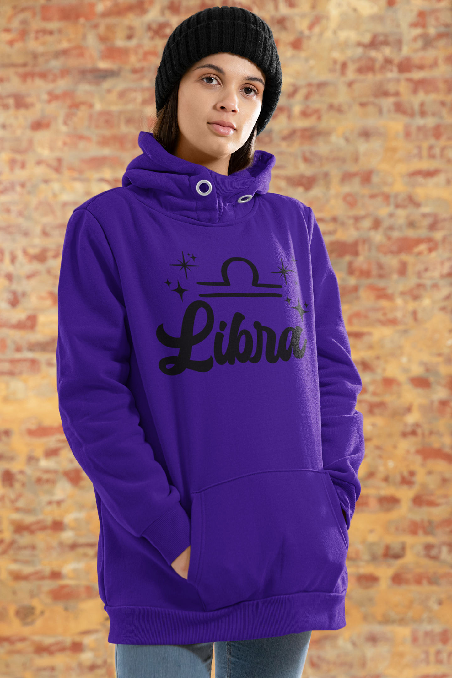 Person wearing a purple hoodie with 'Libra' black text design standing in front of a brick wall.