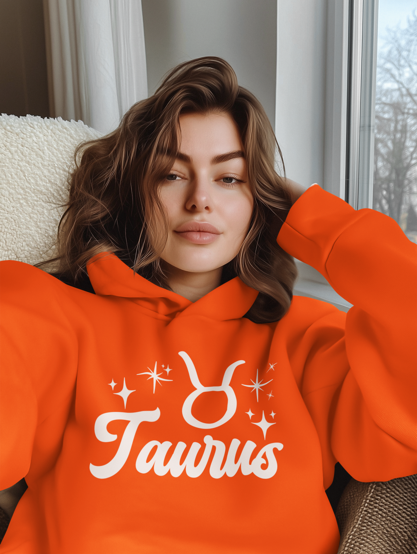 Woman wearing a orange 'Taurus' hoodie with white text design, sitting on a couch.
