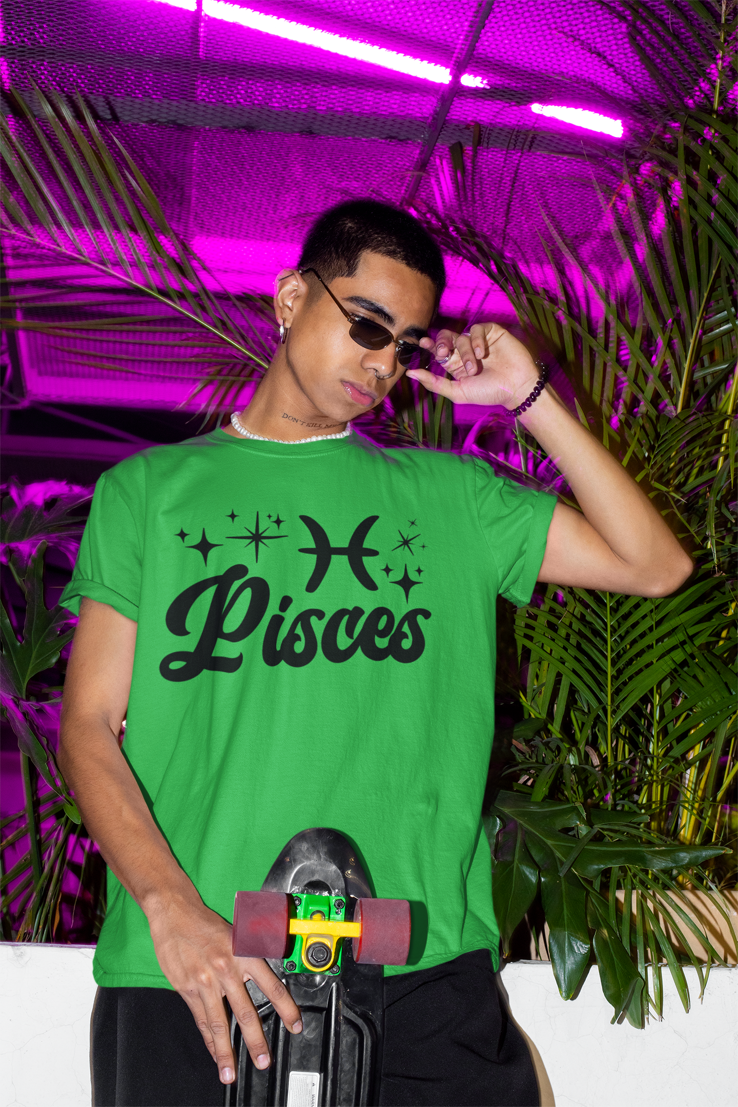 Person wearing a green with black text 'Pisces' t-shirt holding a skateboard with a neon pink background