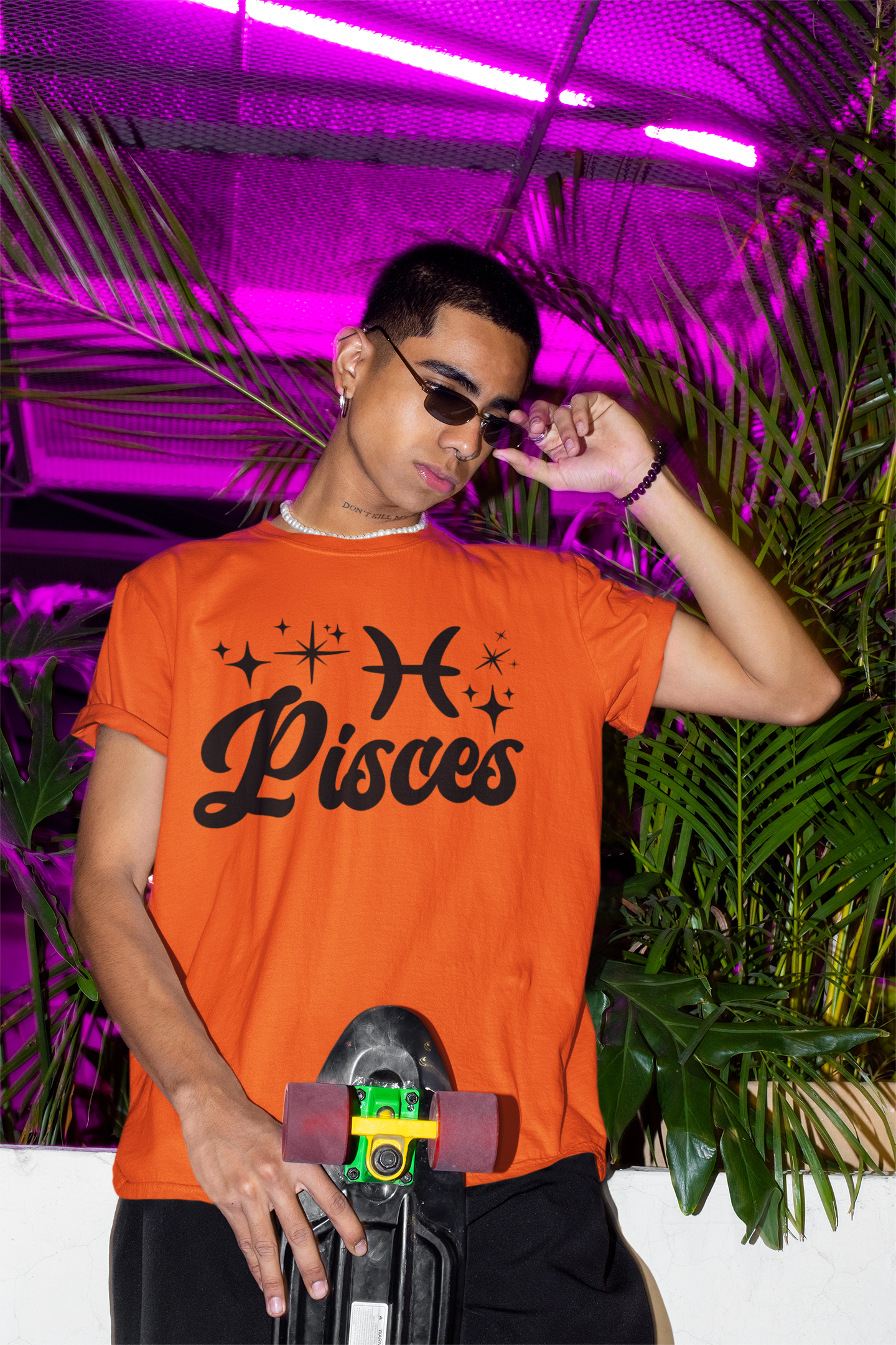 Person wearing a orange with black text 'Pisces' t-shirt holding a skateboard with a neon pink background