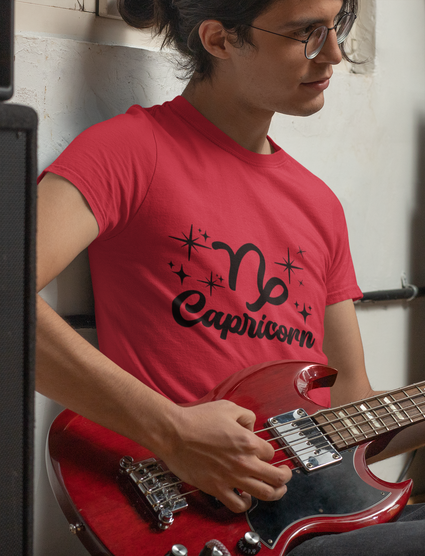 Person wearing a red t-shirt with 'Capricorn' black text design holding a red guitar.