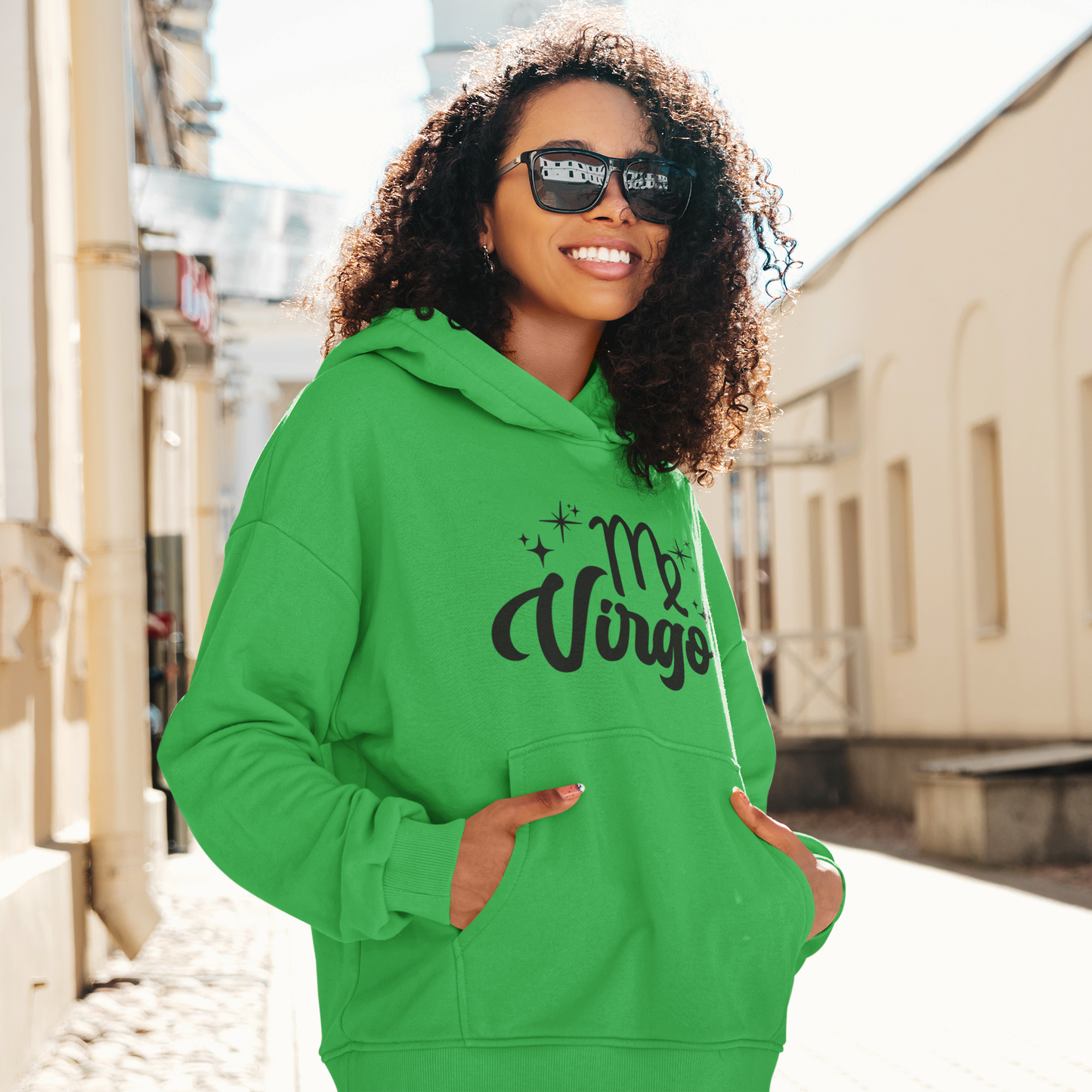 Woman with sunglasses, wearing a green hoodie with "Virgo' black text design standing on the street.