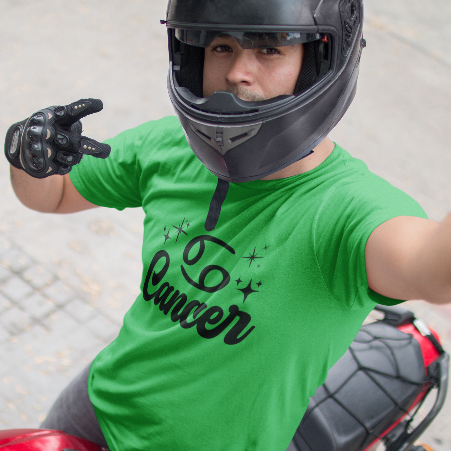 Person wearing a green t-shirt with 'Leo Cancer' black text, black helmet, and gloves on a motorcycle.