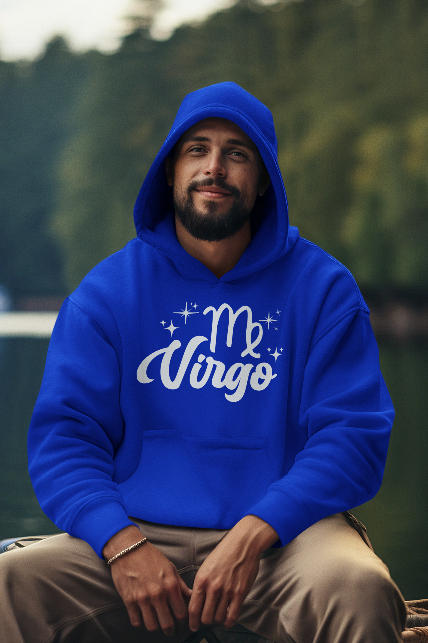 Man wearing a blue hoodie with 'Virgo' white text design, sitting outdoors with a blurred natural background