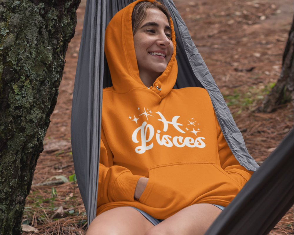 Person sitting in a hammock outdoors wearing a orange hoodie with 'Pisces' white text with zodiac symbol.