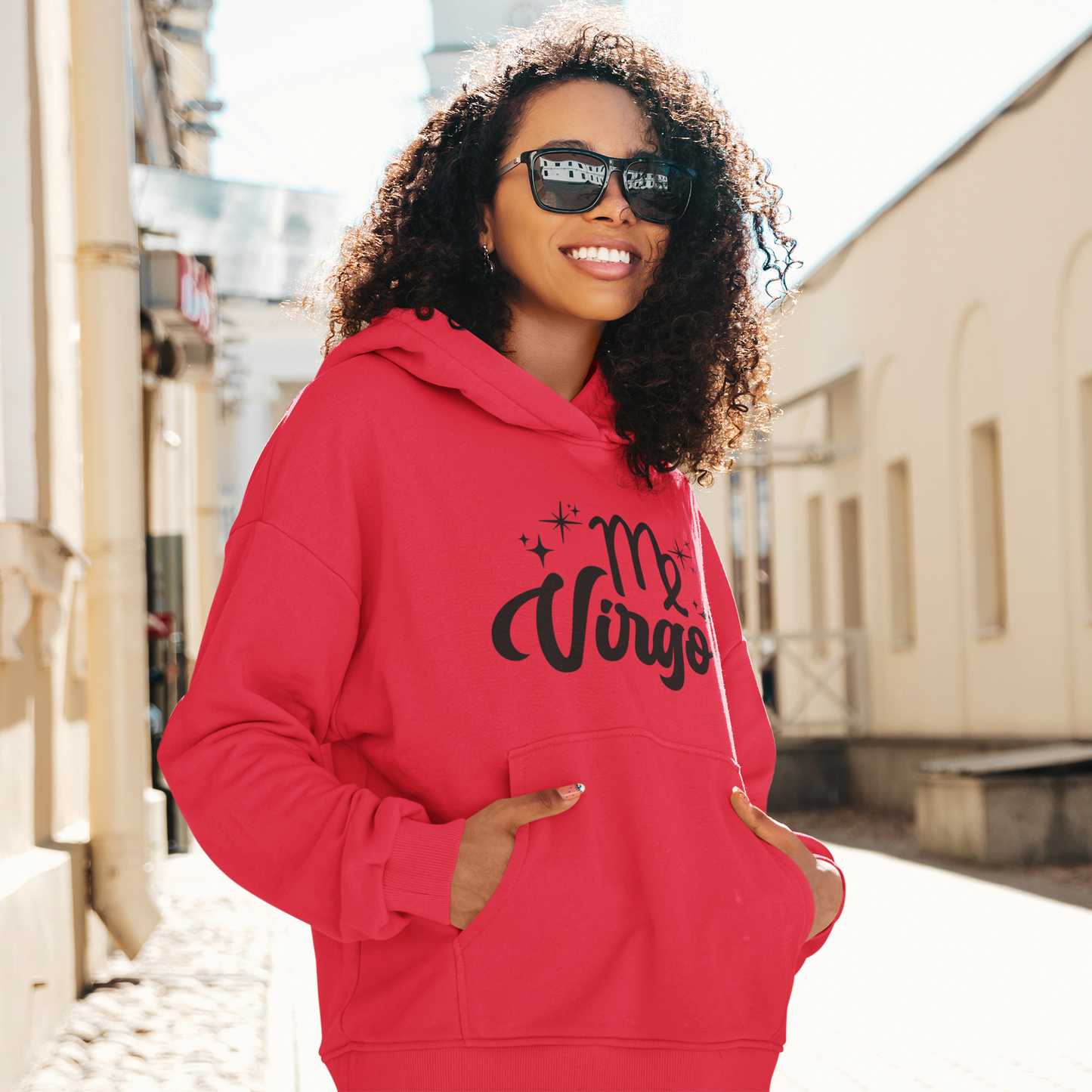 Woman with sunglasses, wearing a red hoodie with "Virgo' black text design standing on the street.