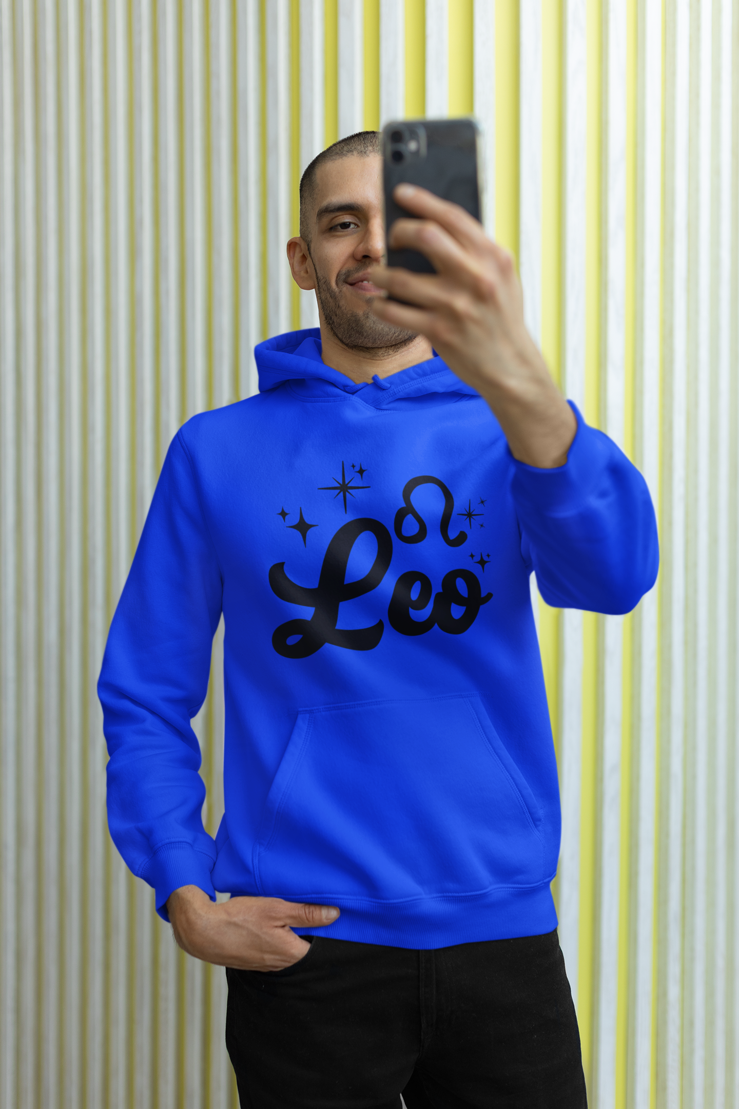 Person wearing a blue hoodie with 'Leo' black text, taking a selfie against a striped wall.