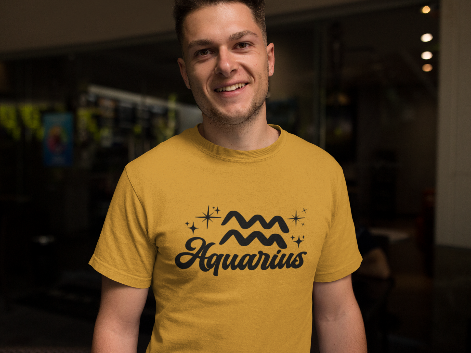 Person wearing a gold t-shirt with 'Aquarius' black text design in a dark indoor setting