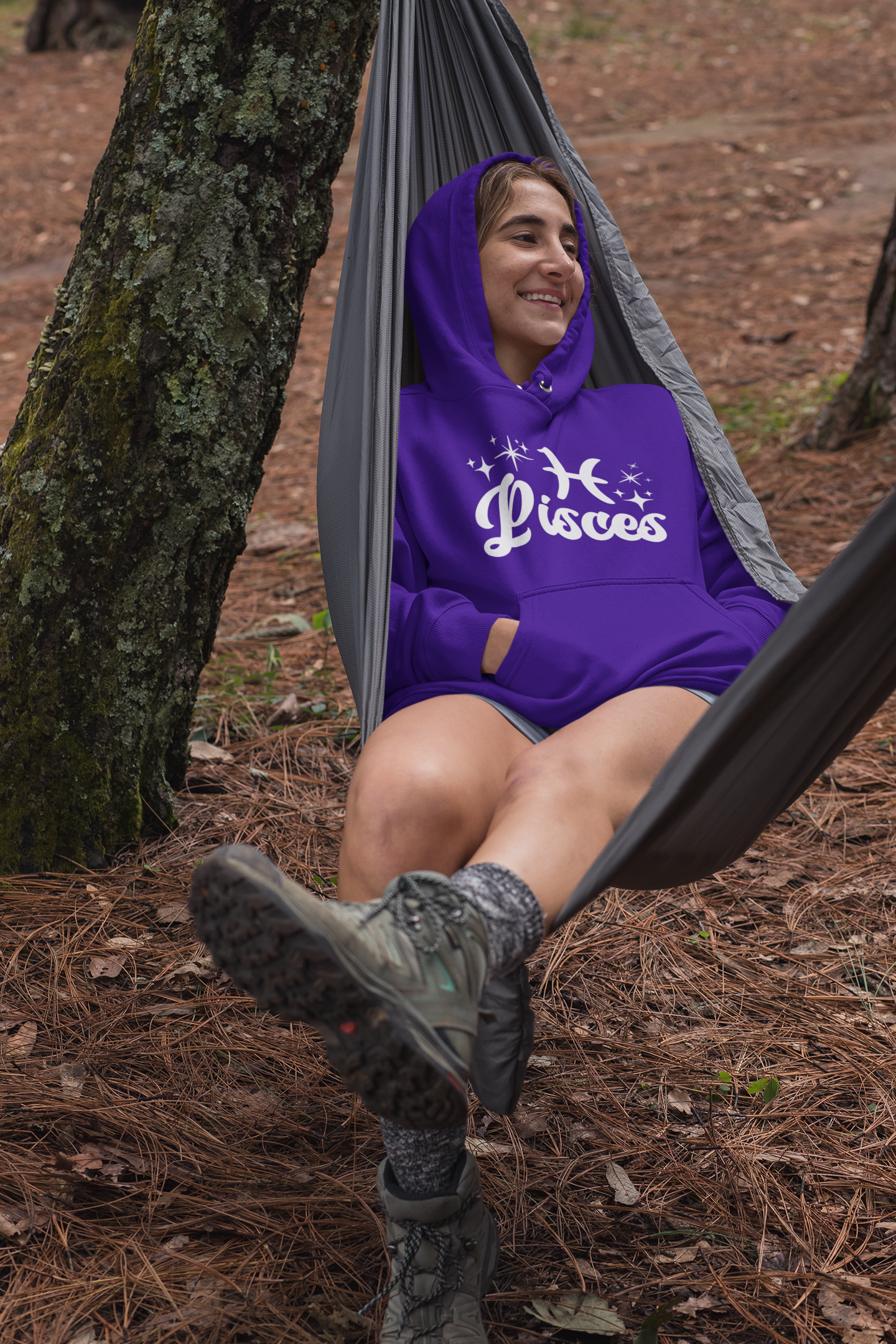 Person sitting in a hammock outdoors wearing a purple hoodie with 'Pisces' white text with zodiac symbol.