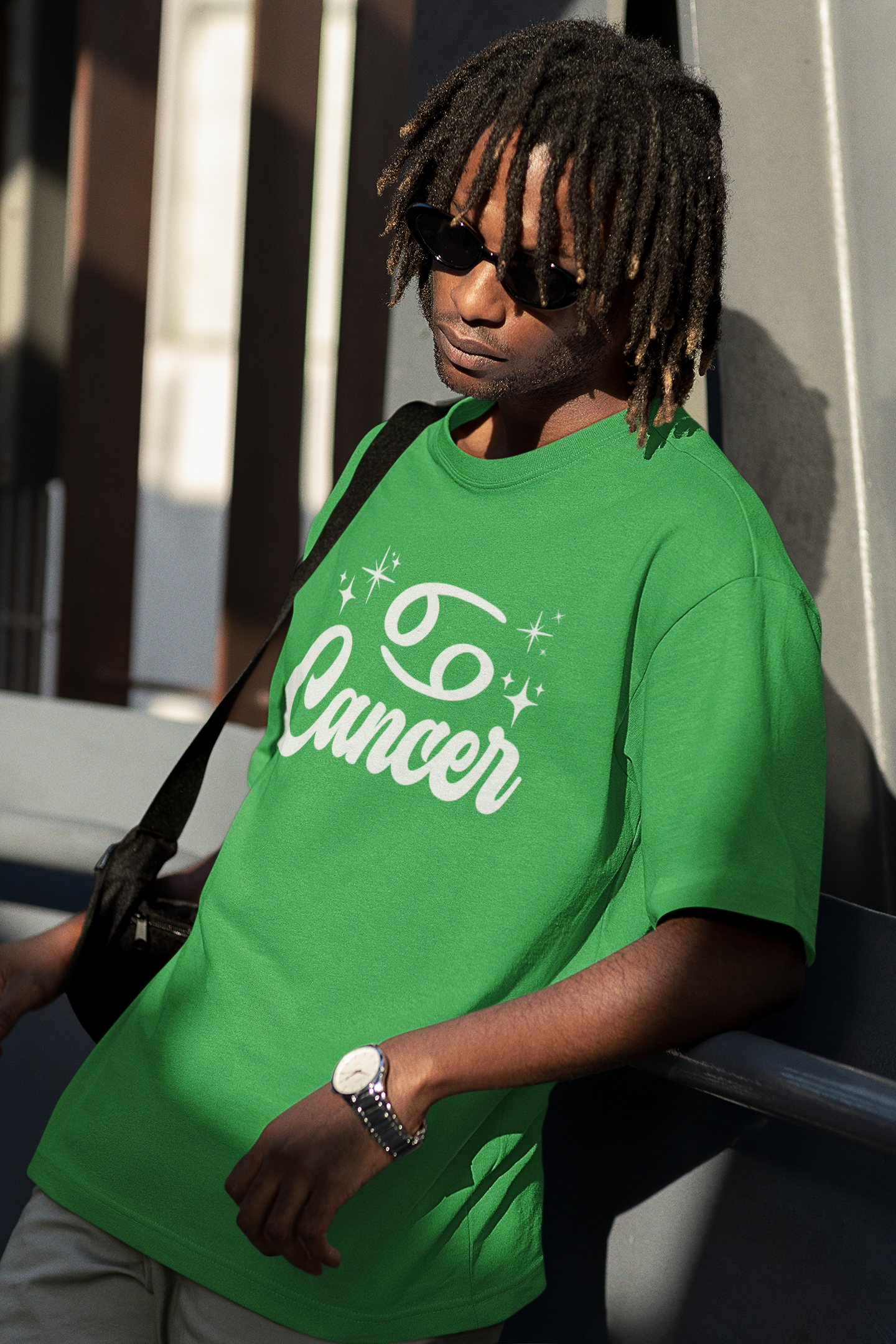 Person wearing a green t-shirt with 'Cancer' white text design, standing against a building.