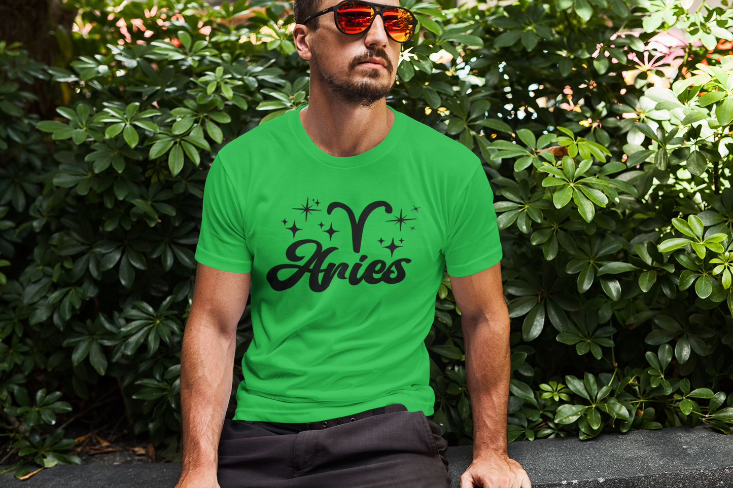 Man wearing an green t-shirt with 'Aries' black text design sitting outdoors.