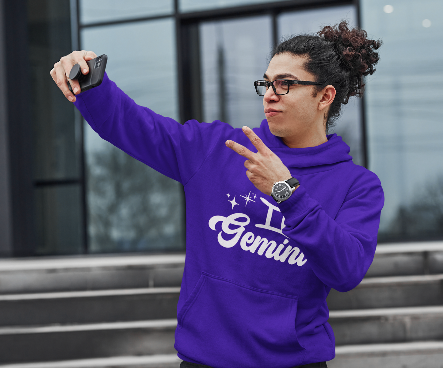 Person wearing an purple hoodie with 'Gemini' white text, taking a selfie outdoors.