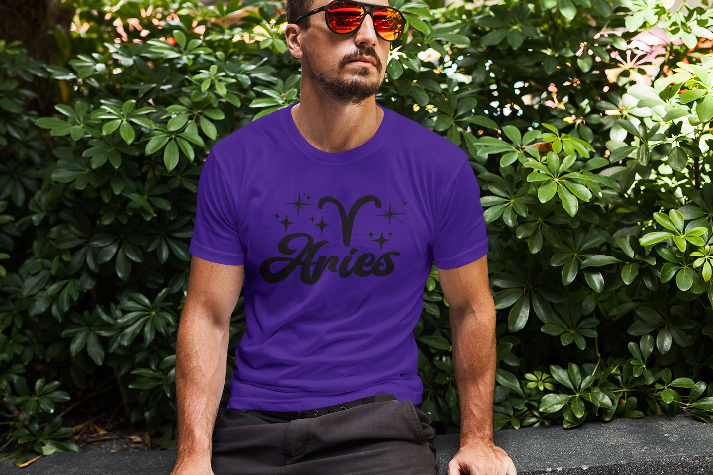 Man wearing an purple t-shirt with 'Aries' black text design sitting outdoors.