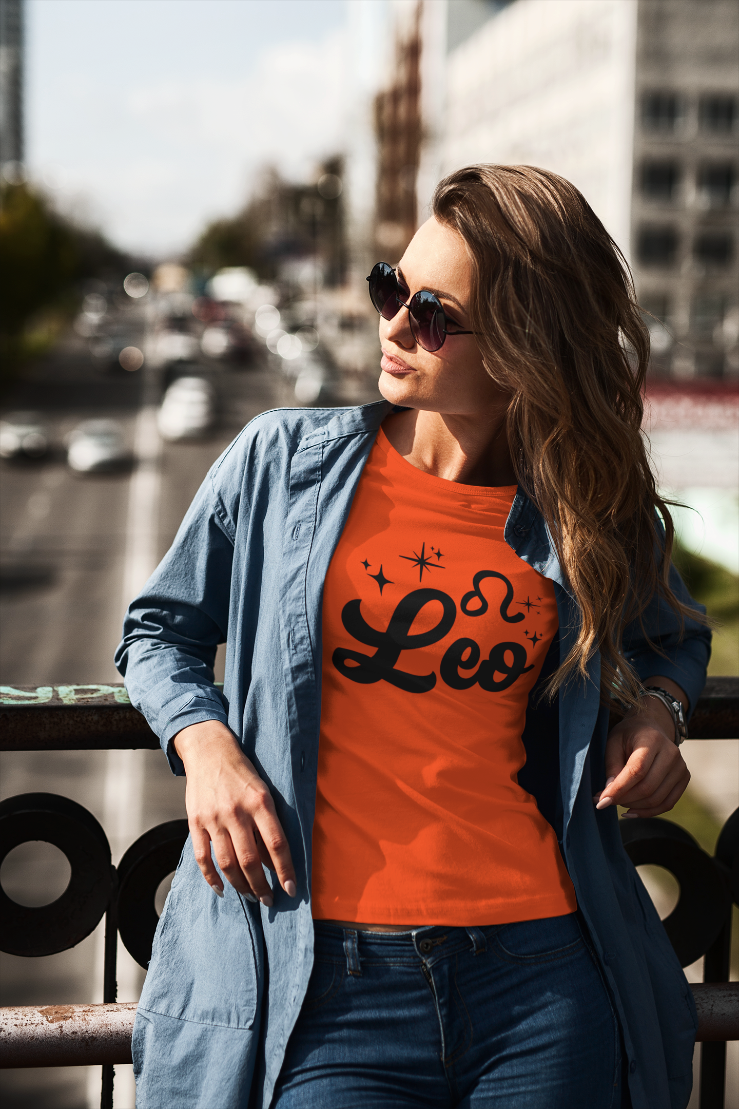Woman wearing a orange t-shirt with 'Leo' black text design standing on a overpass.