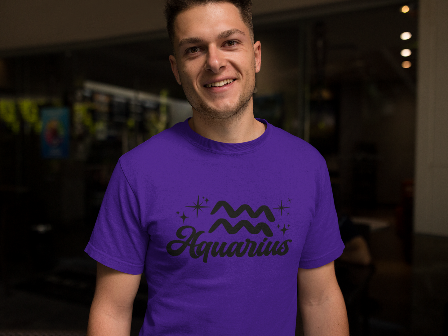 Person wearing a purple t-shirt with 'Aquarius' black text design in a dark indoor setting