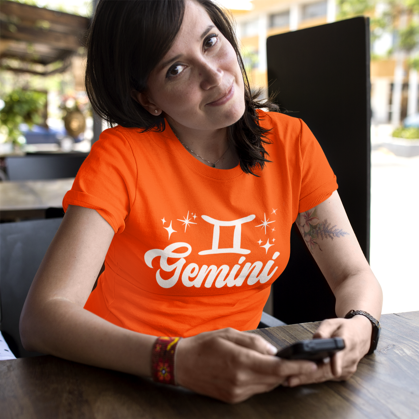 Person wearing a orange t-shirt with 'Gemini' white text design sitting at a table.