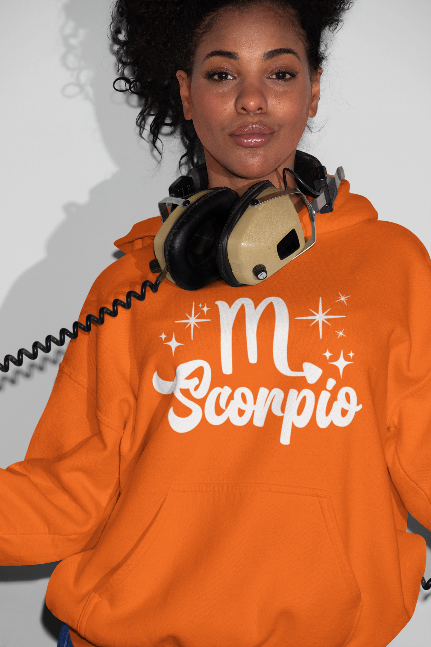 Person wearing a orange hoodie with 'Scorpio' white text design, with headphones 