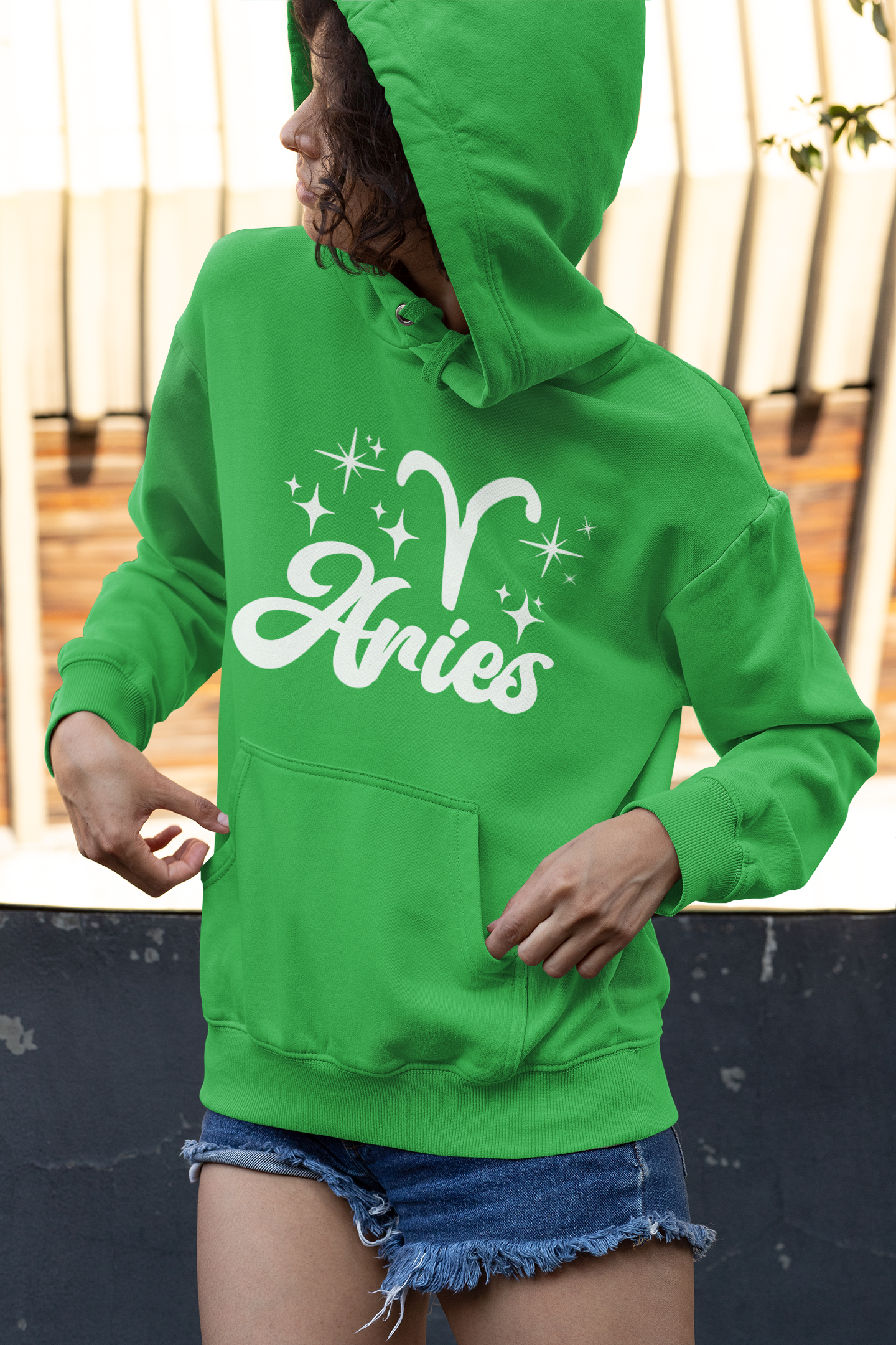 Person wearing a green hoodie with 'Aries with zodiac symbol' white text, standing outdoors.