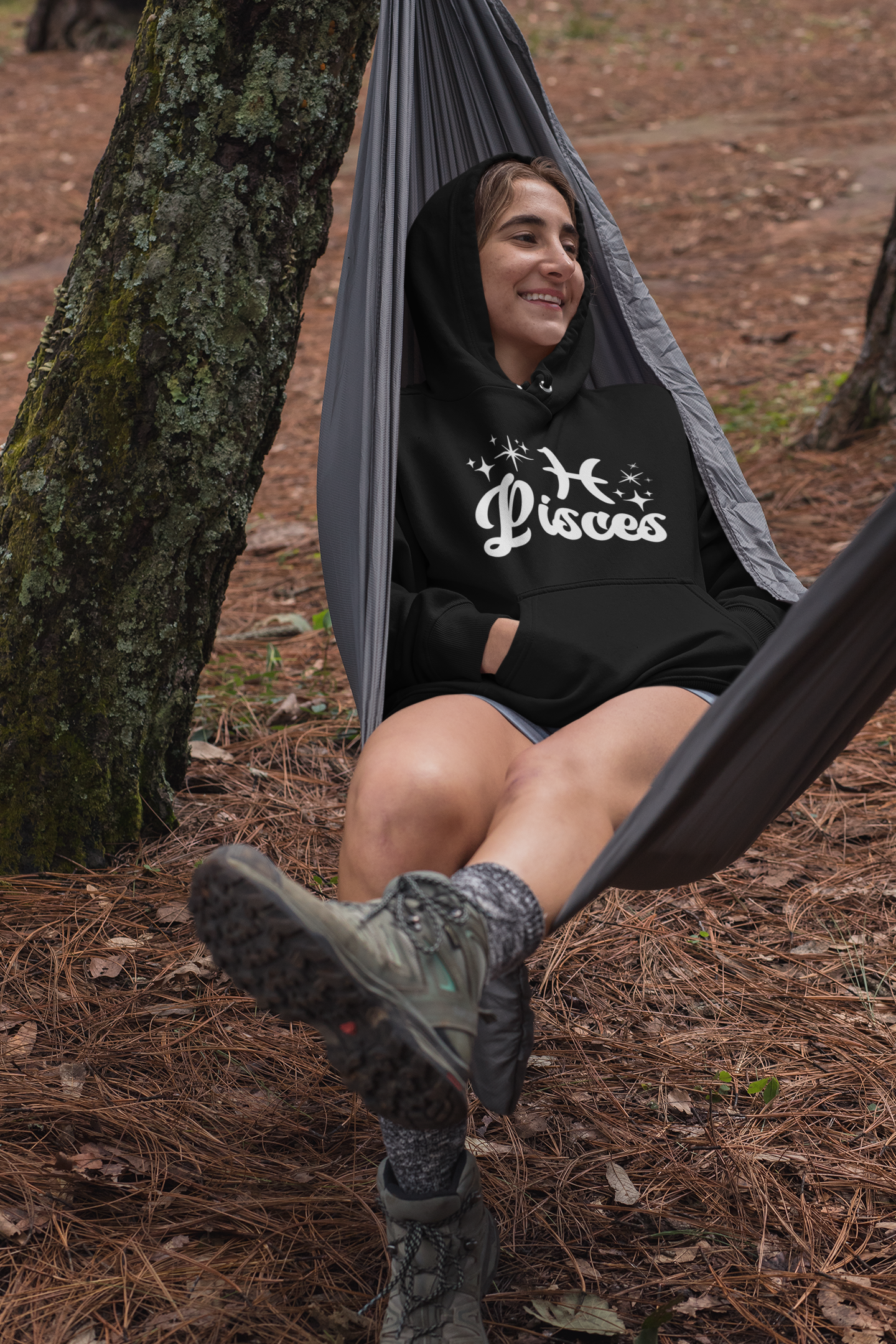 Person sitting in a hammock outdoors wearing a black hoodie with 'Pisces' white text with zodiac symbol.