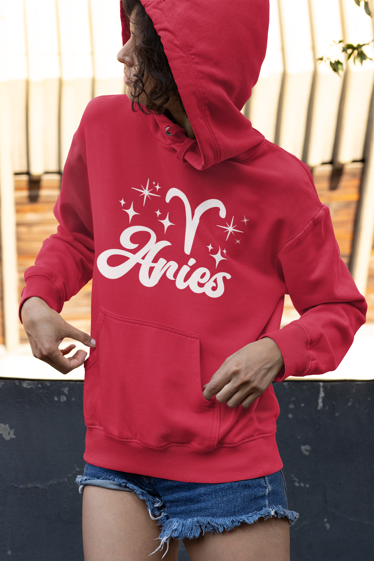 Person wearing a red hoodie with 'Aries with zodiac symbol' white text, standing outdoors.