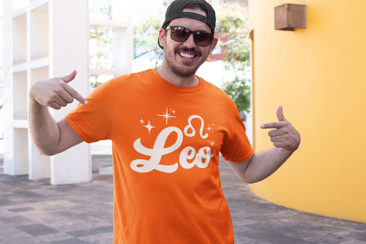 Man wearing a orange t-shirt with 'Leo' white text design, giving thumbs up outdoors.
