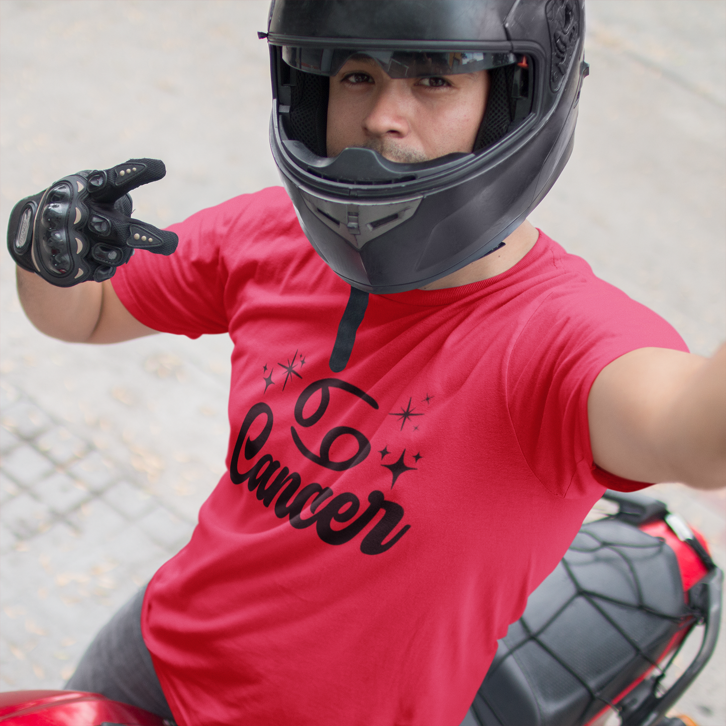 Person wearing a red t-shirt with 'Leo Cancer' black text, black helmet, and gloves on a motorcycle.
