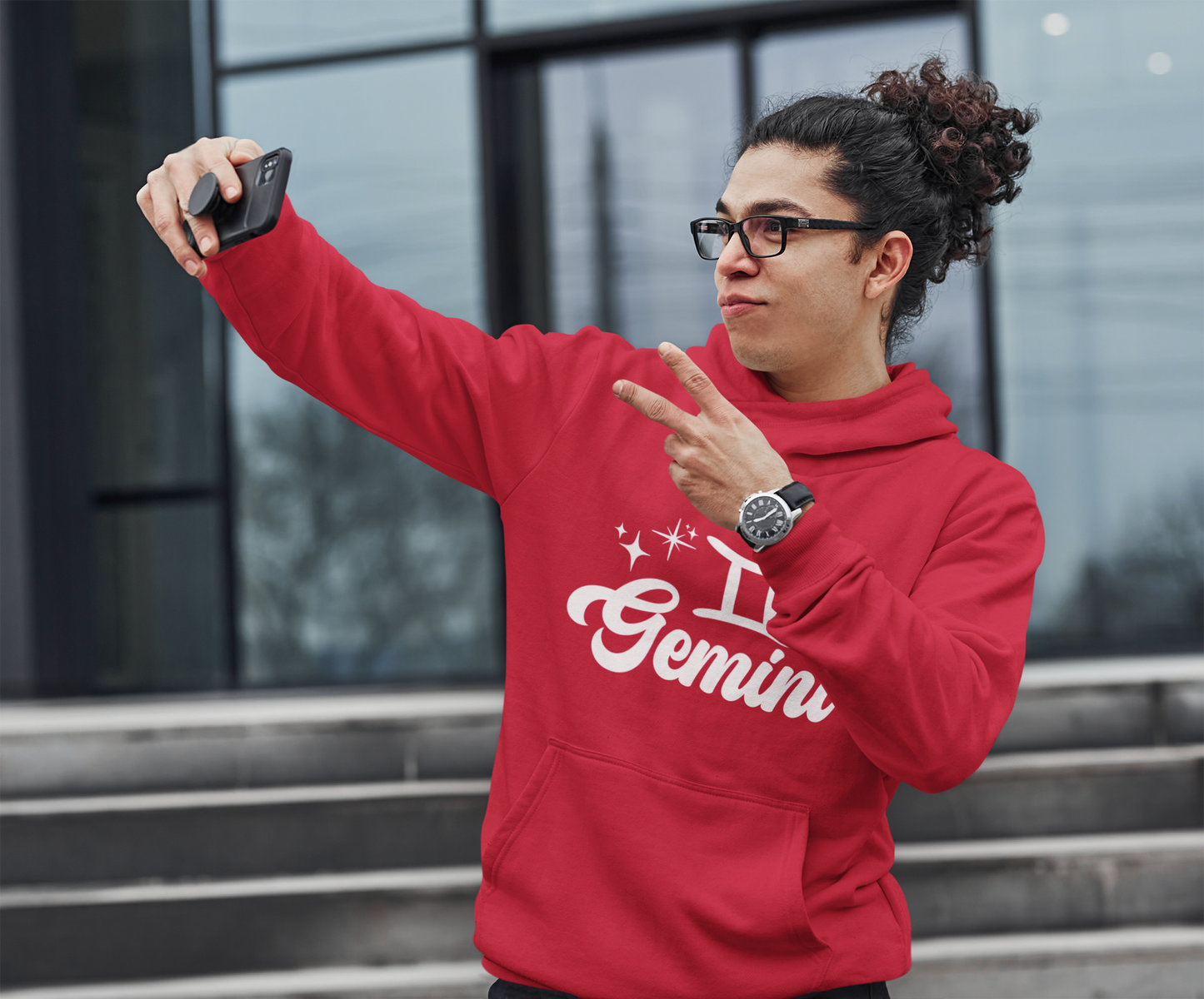 Person wearing an red hoodie with 'Gemini' white text, taking a selfie outdoors.