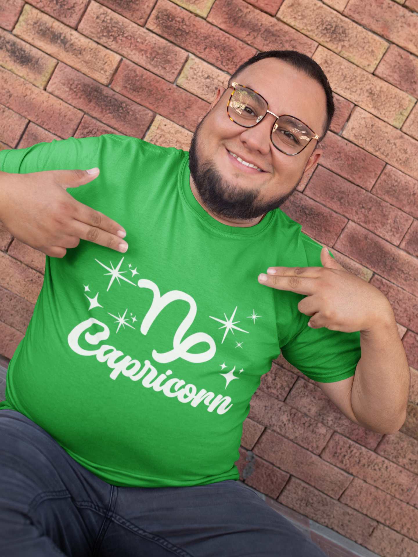 Man wearing a green t-shirt with 'Capricorn' white text design, pointing at it, against a brick wall.