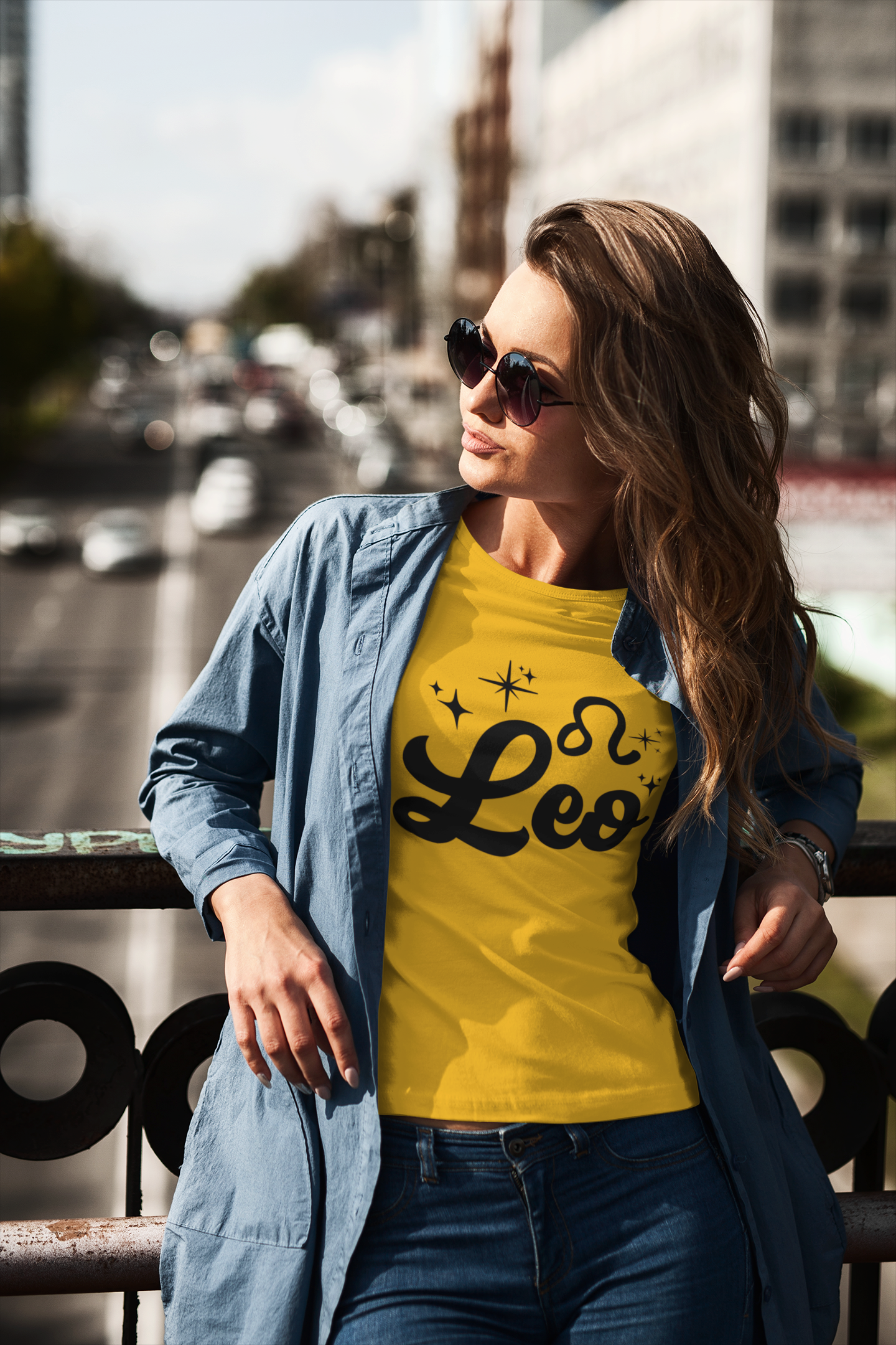 Woman wearing a gold t-shirt with 'Leo' black text design standing on a overpass.