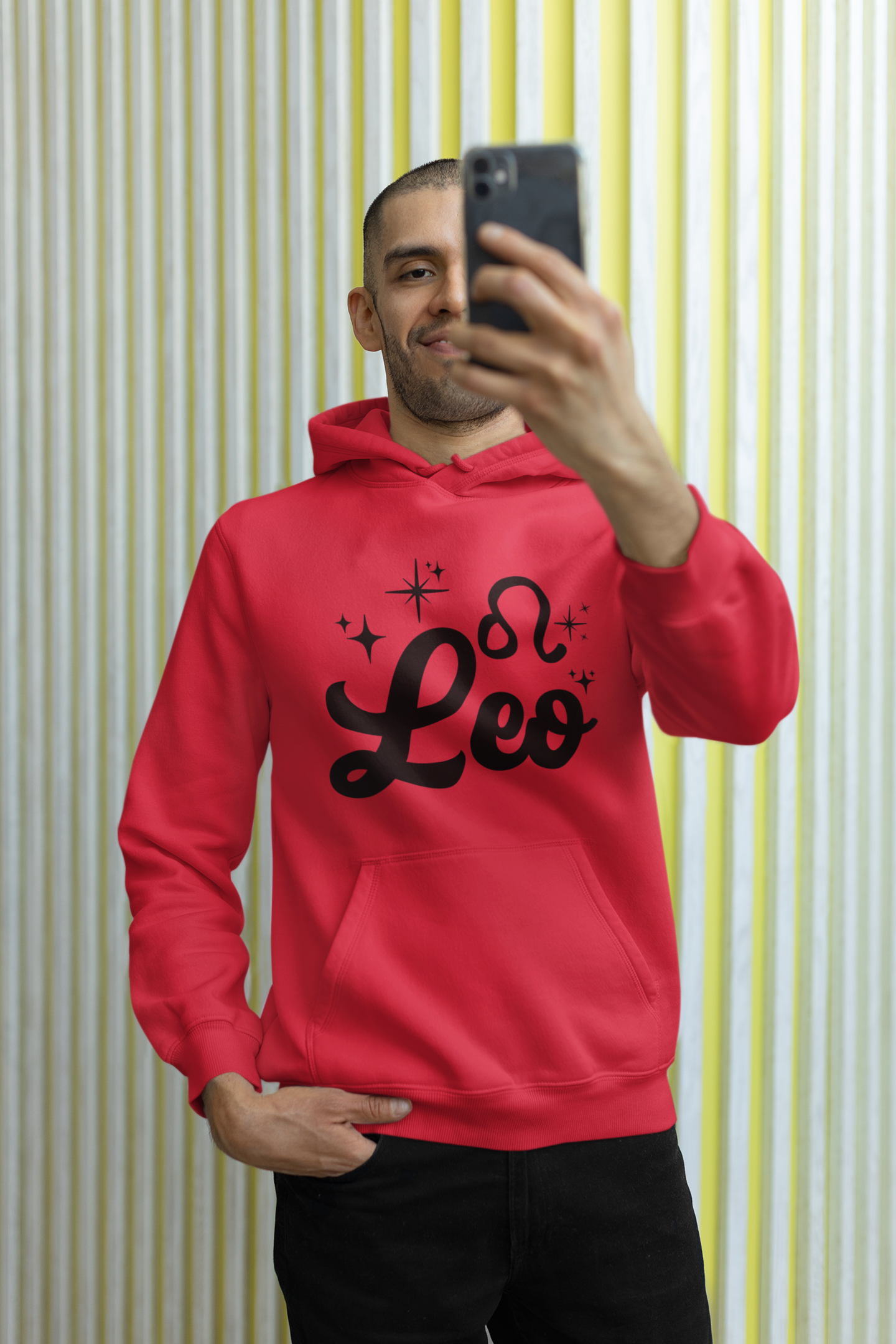 Person wearing a red hoodie with 'Leo' black text, taking a selfie against a striped wall.