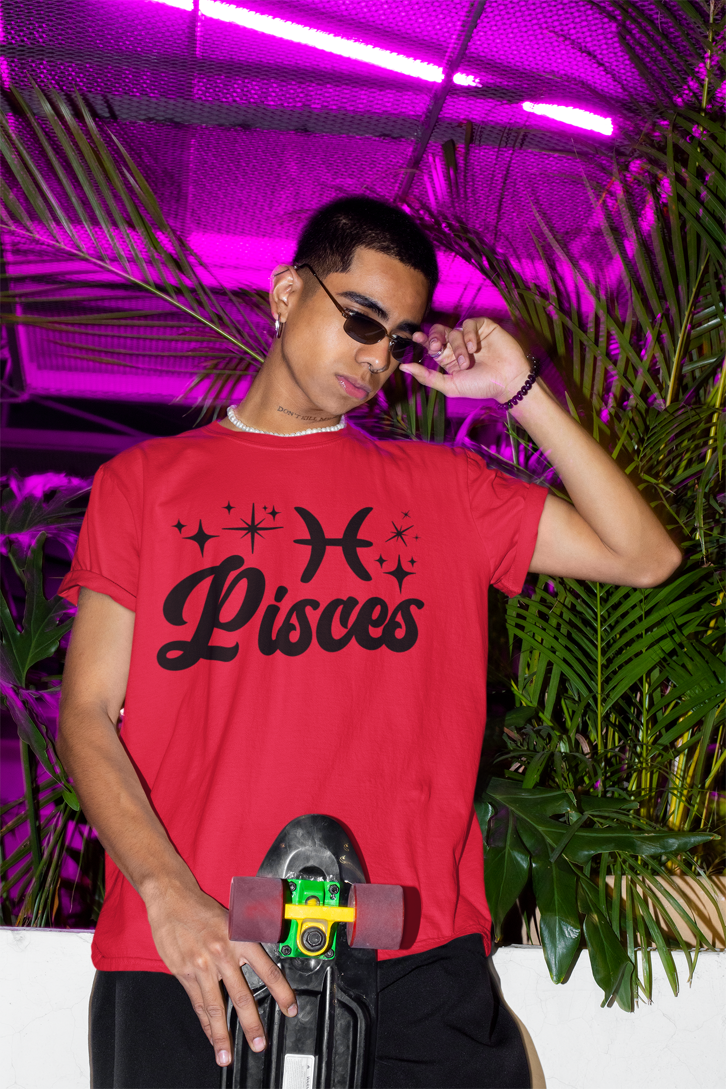 Person wearing a red with black text 'Pisces' t-shirt holding a skateboard with a neon pink background
