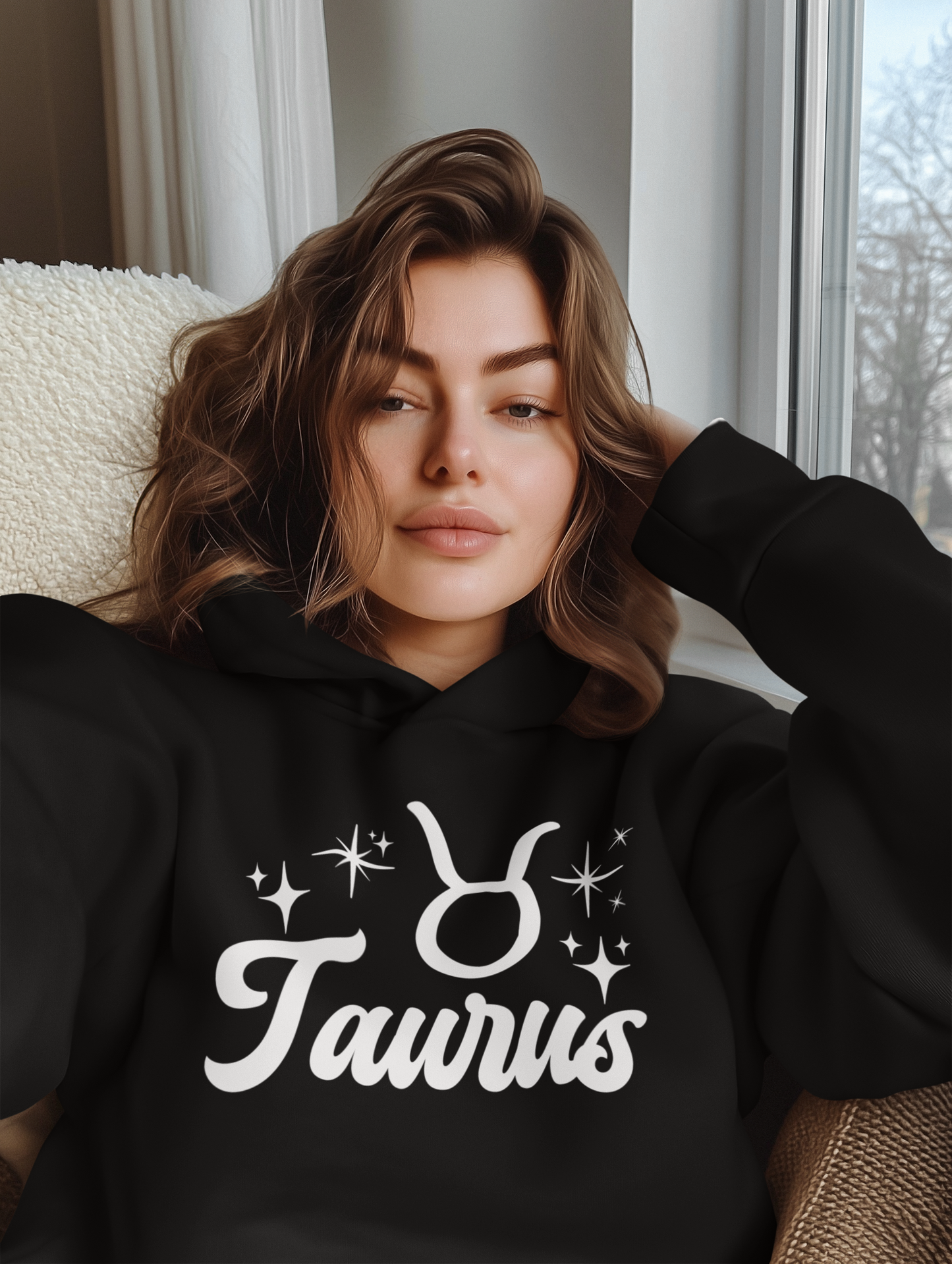 Woman wearing a black 'Taurus' hoodie with white text design, sitting on a couch.