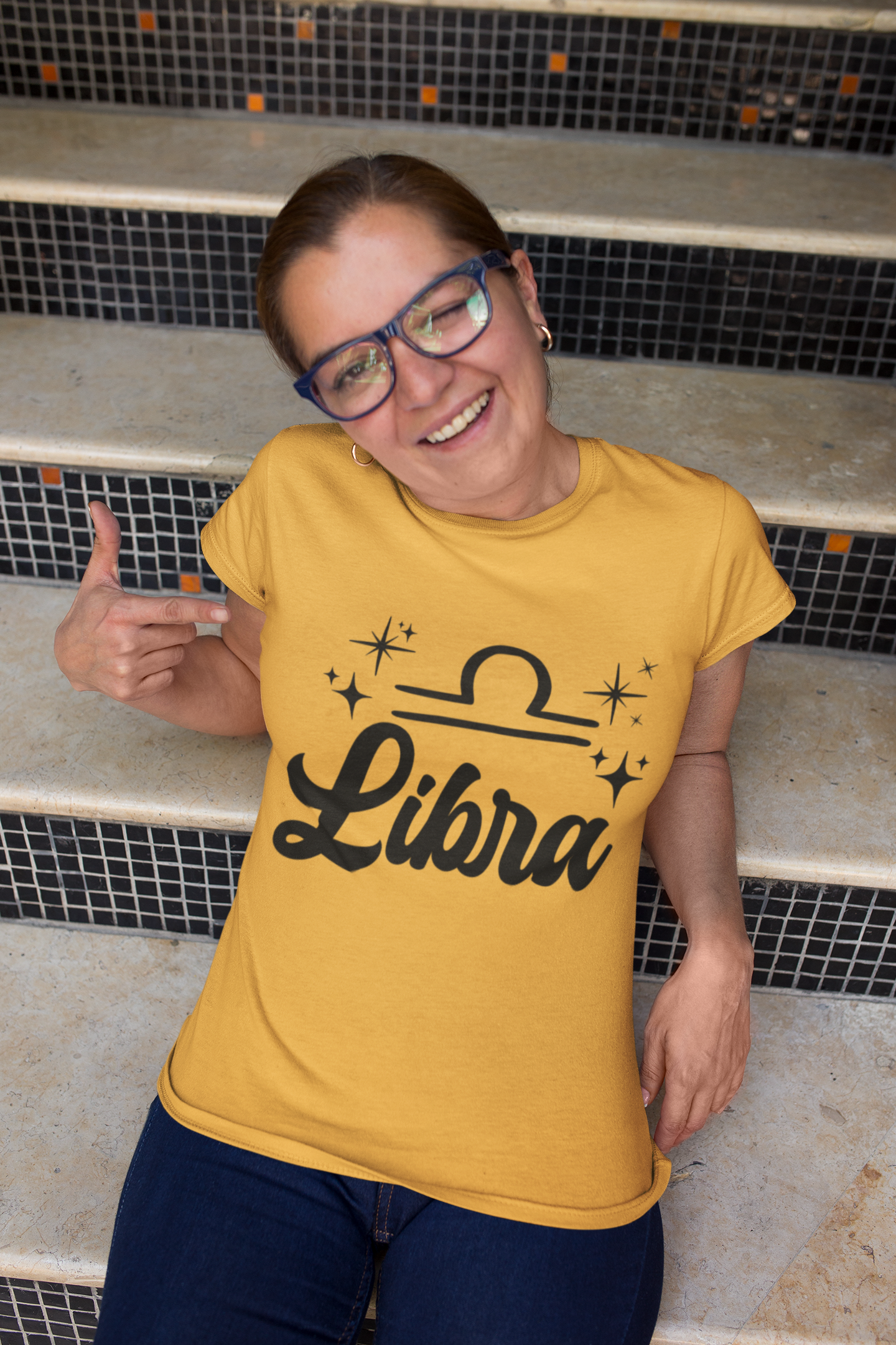 Person wearing a gold 'Libra' black text design t-shirt sitting on steps.