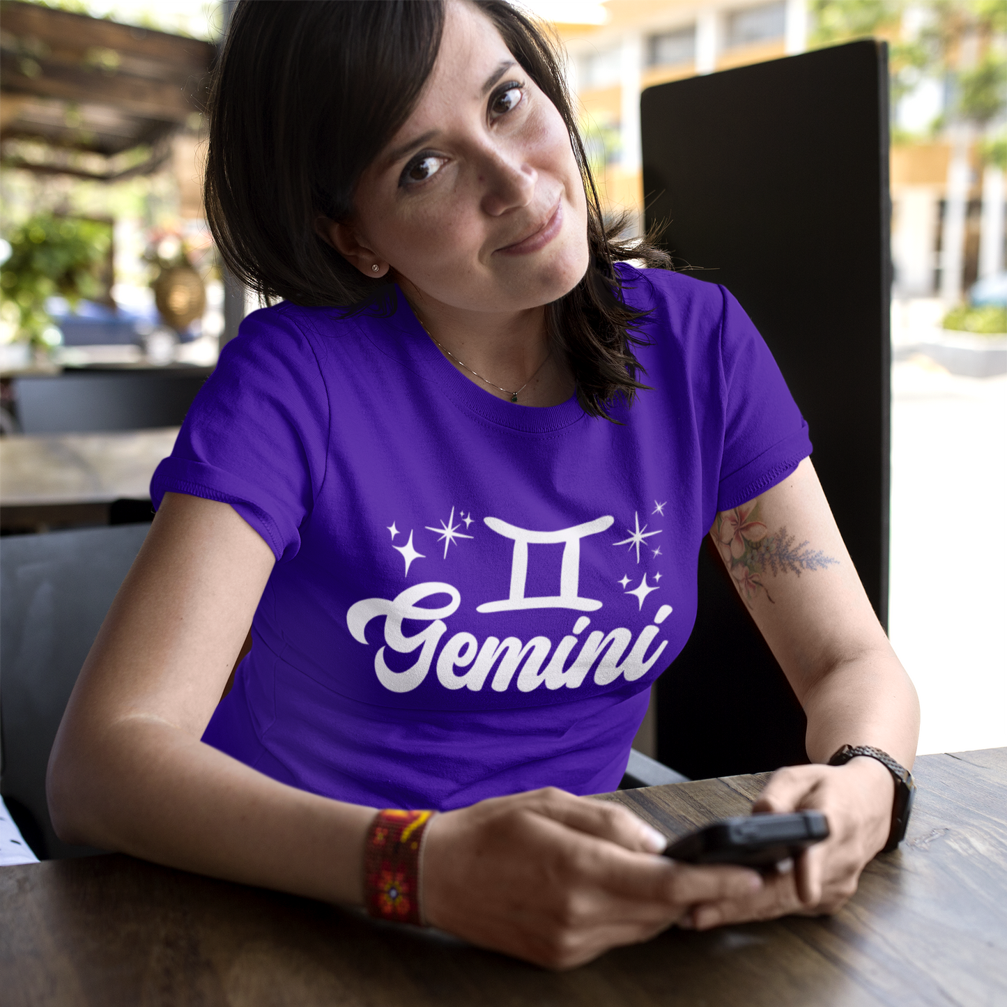 Person wearing a purple t-shirt with 'Gemini' white text design sitting at a table.