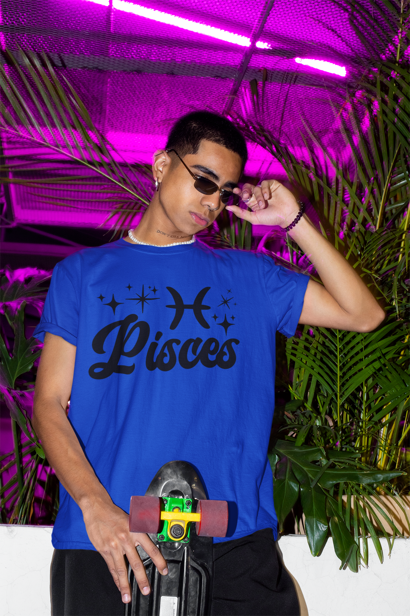 Person wearing a blue with black text 'Pisces' t-shirt holding a skateboard with a neon pink background