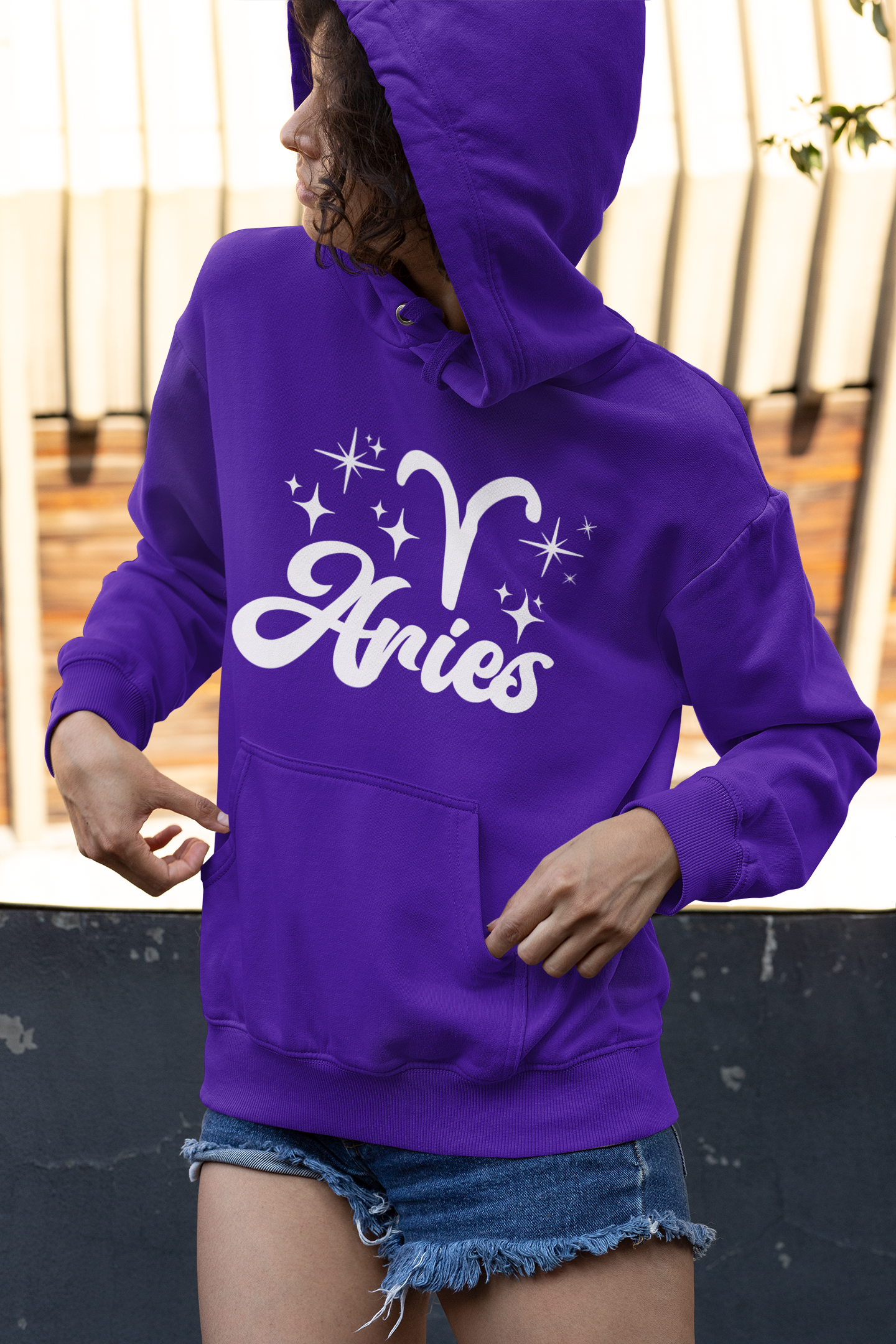 Person wearing a purple hoodie with 'Aries with zodiac symbol' white text, standing outdoors.
