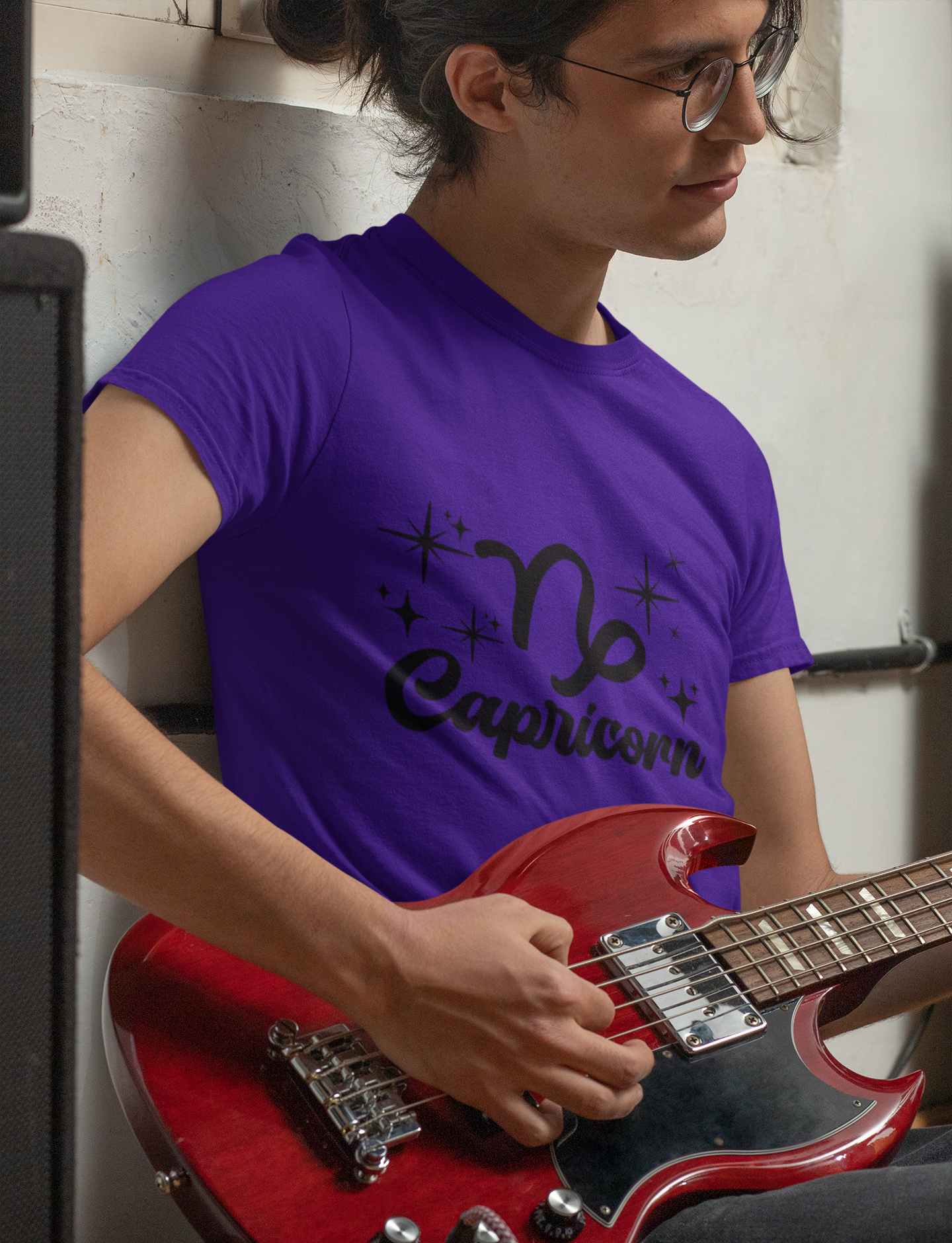 Person wearing a purple t-shirt with 'Capricorn' black text design holding a red guitar.