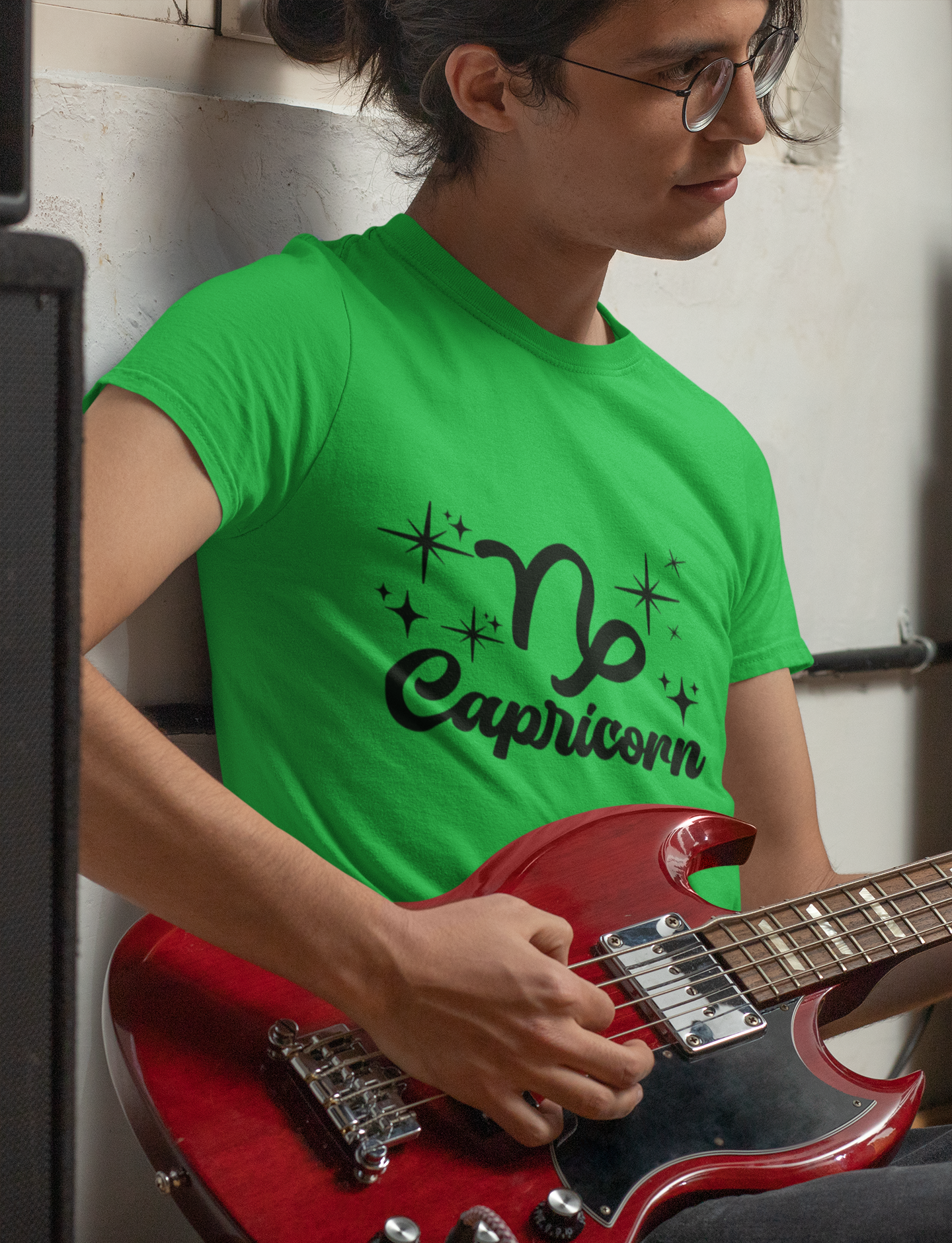Person wearing a green t-shirt with 'Capricorn' black text design holding a red guitar.