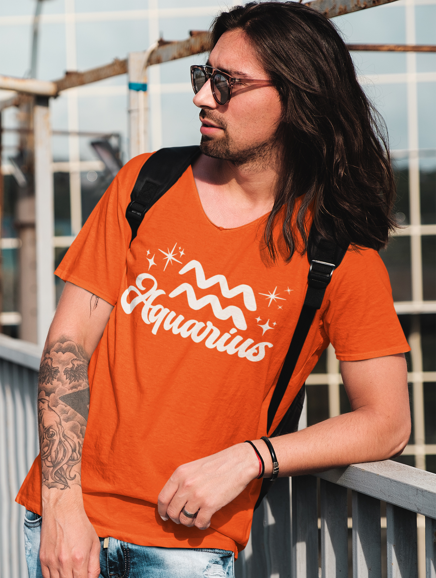 Person wearing a orange 'Aquarius' t-shirt - white text design, with sunglasses and a backpack.