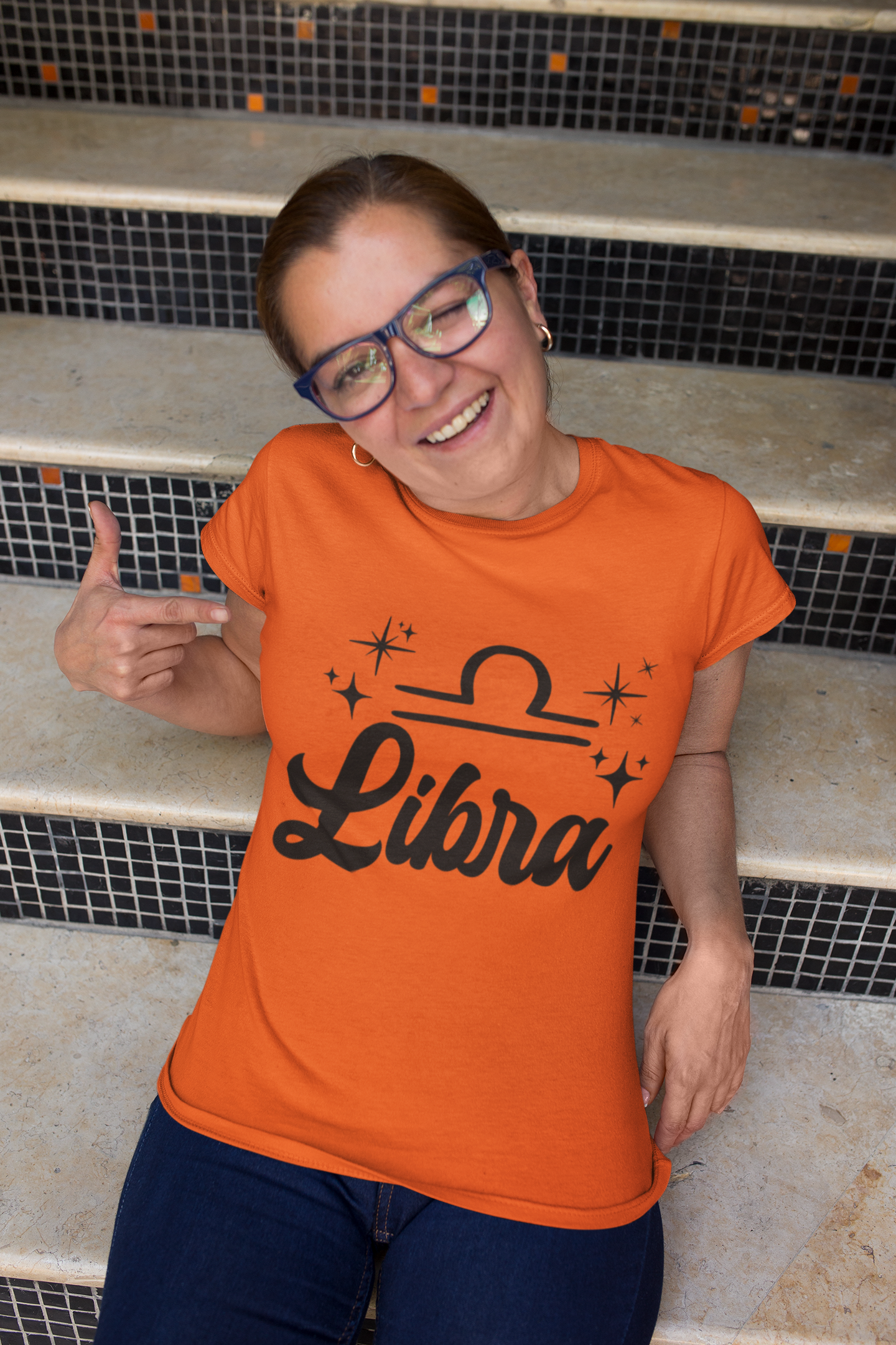 Person wearing a orange 'Libra' black text design t-shirt sitting on steps.
