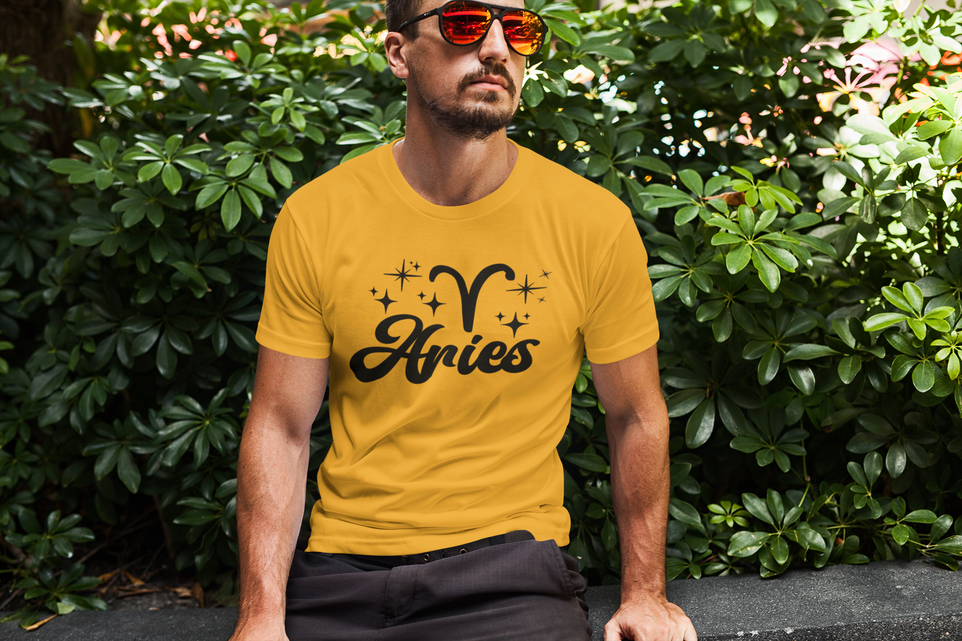Man wearing an gold t-shirt with 'Aries' black text design sitting outdoors.