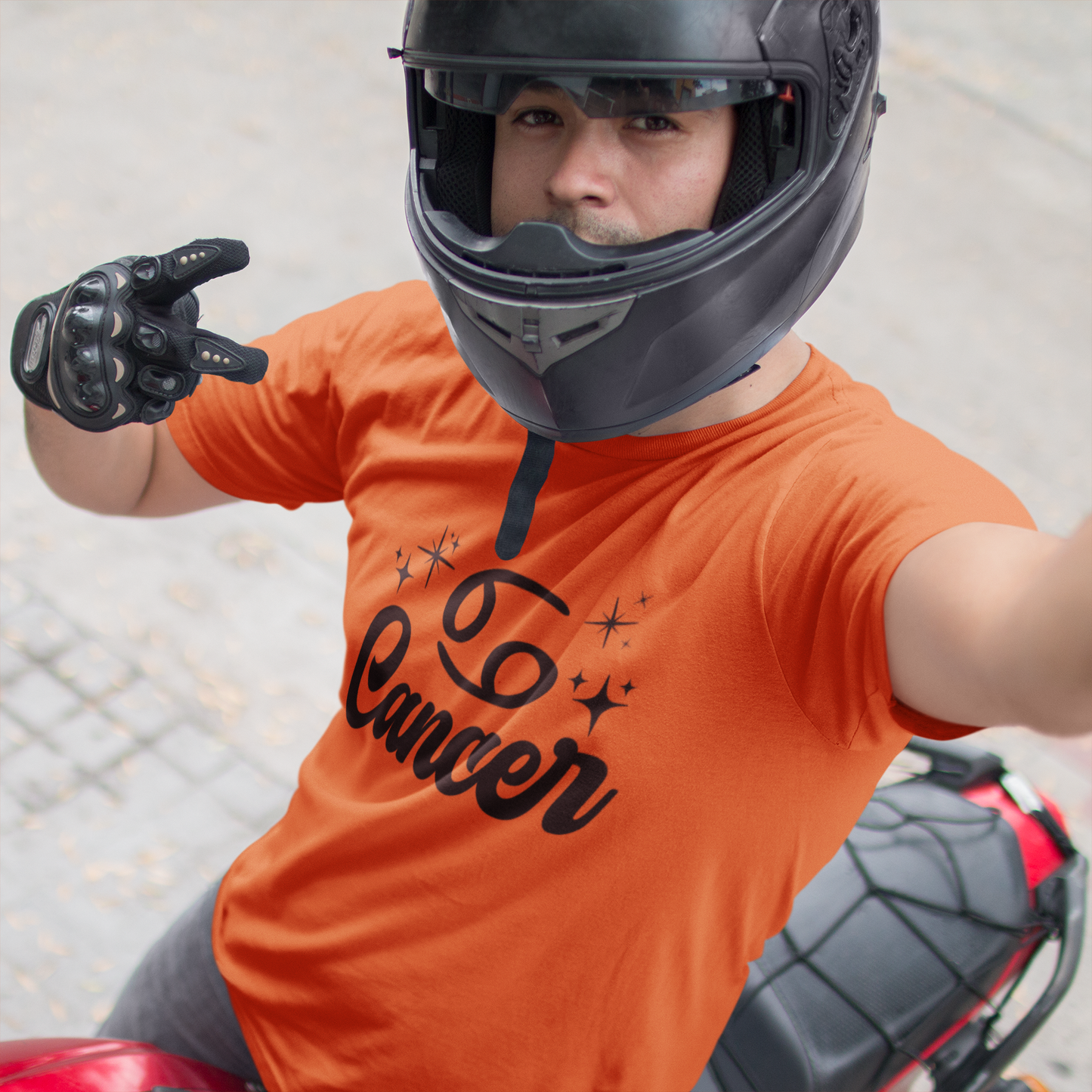 Person wearing a orange t-shirt with 'Leo Cancer' black text, black helmet, and gloves on a motorcycle.