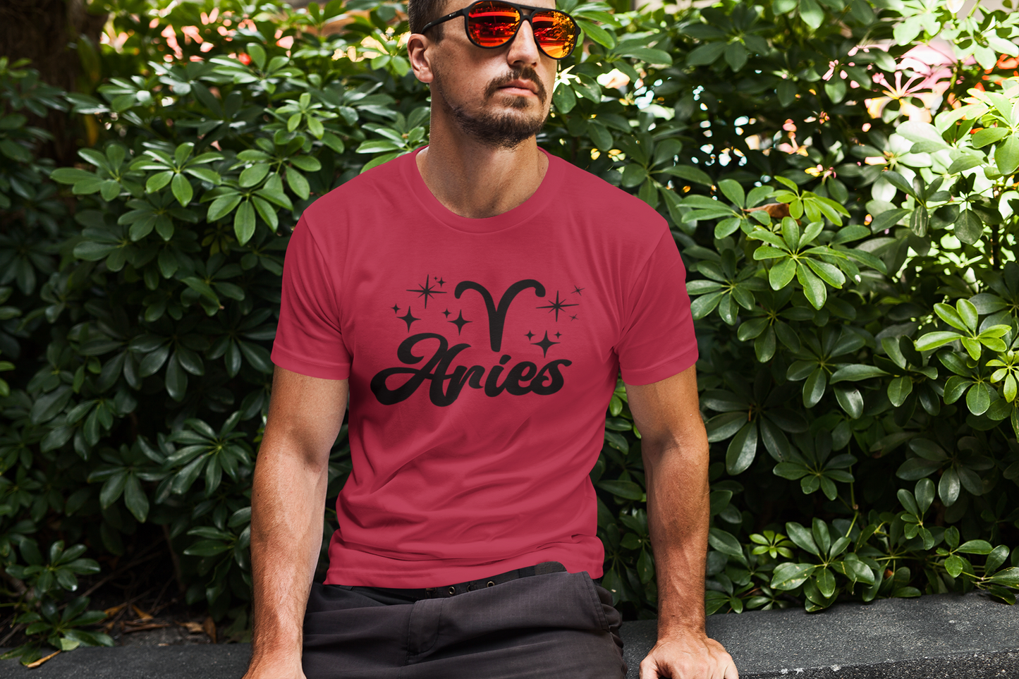 Man wearing an red t-shirt with 'Aries' black text design sitting outdoors.