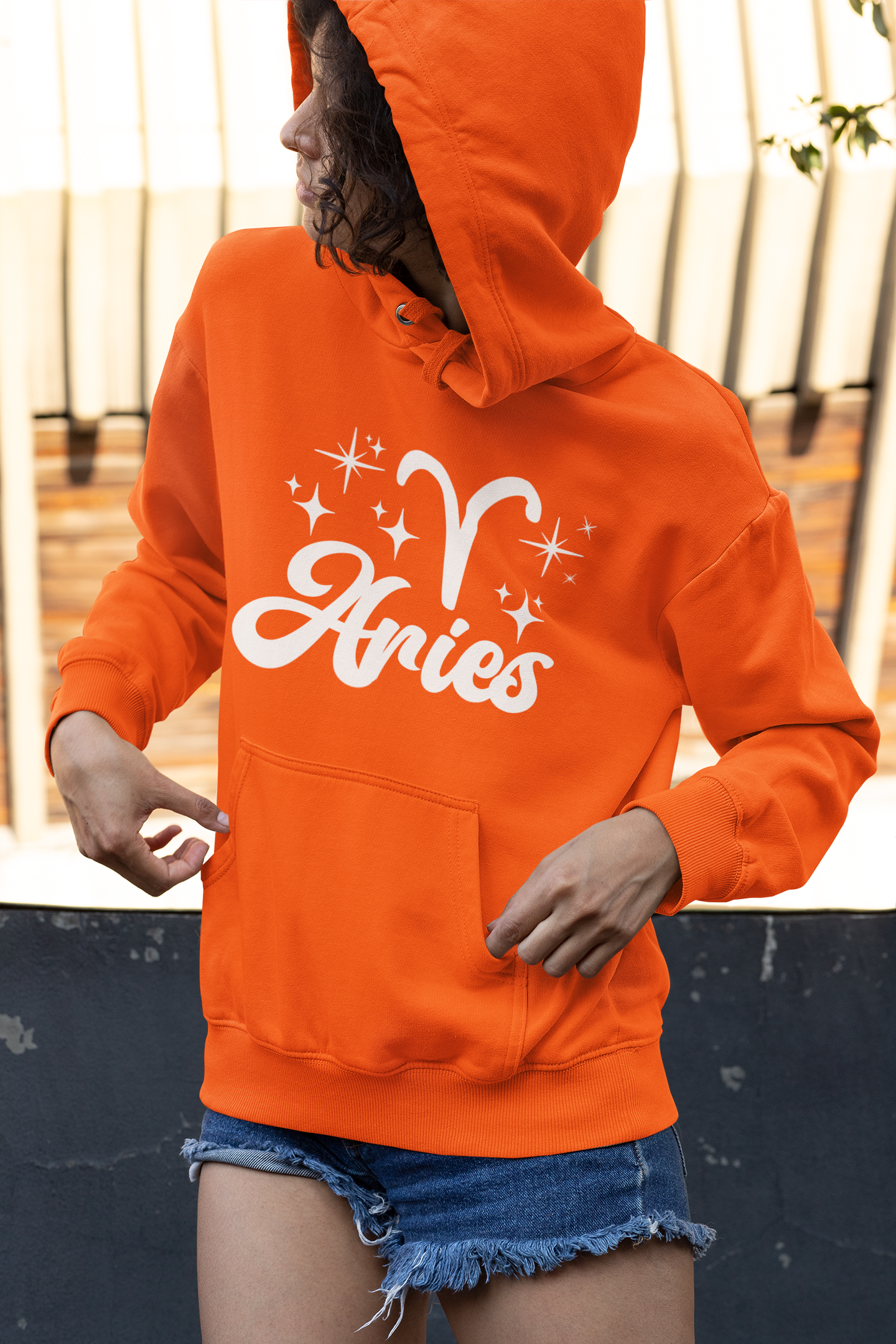 Person wearing a orange hoodie with 'Aries with zodiac symbol' white text, standing outdoors.