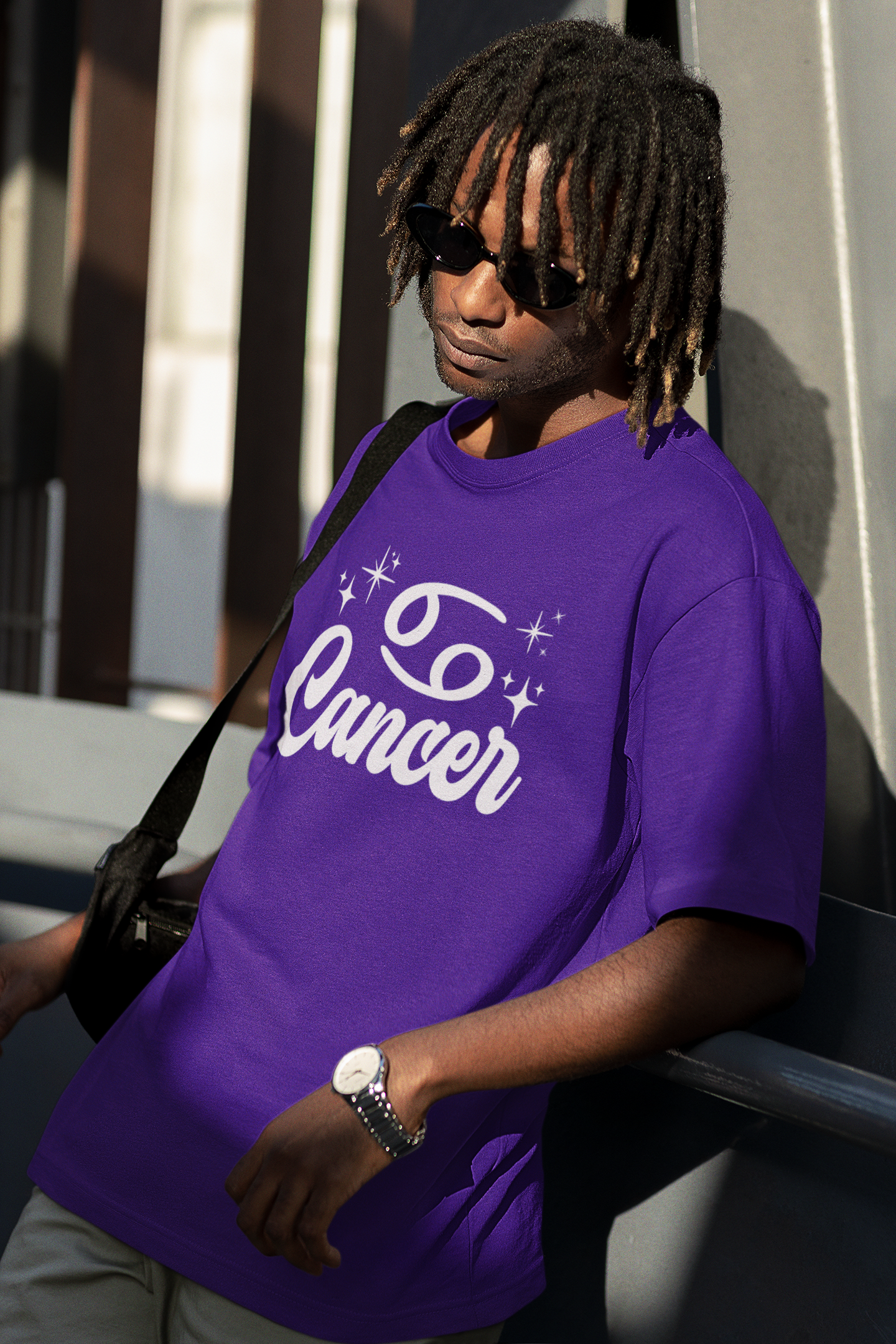 Person wearing a purple t-shirt with 'Cancer' white text design, standing against a building.